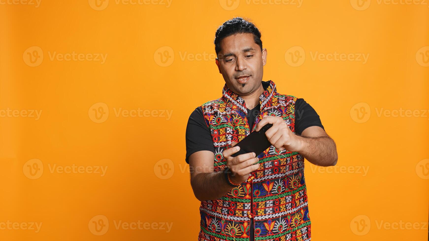 Cheerful Indian person in traditional clothing entertained by videogames on smartphone. Joyous player enjoying game on phone, having fun online, studio backdrop, camera B photo