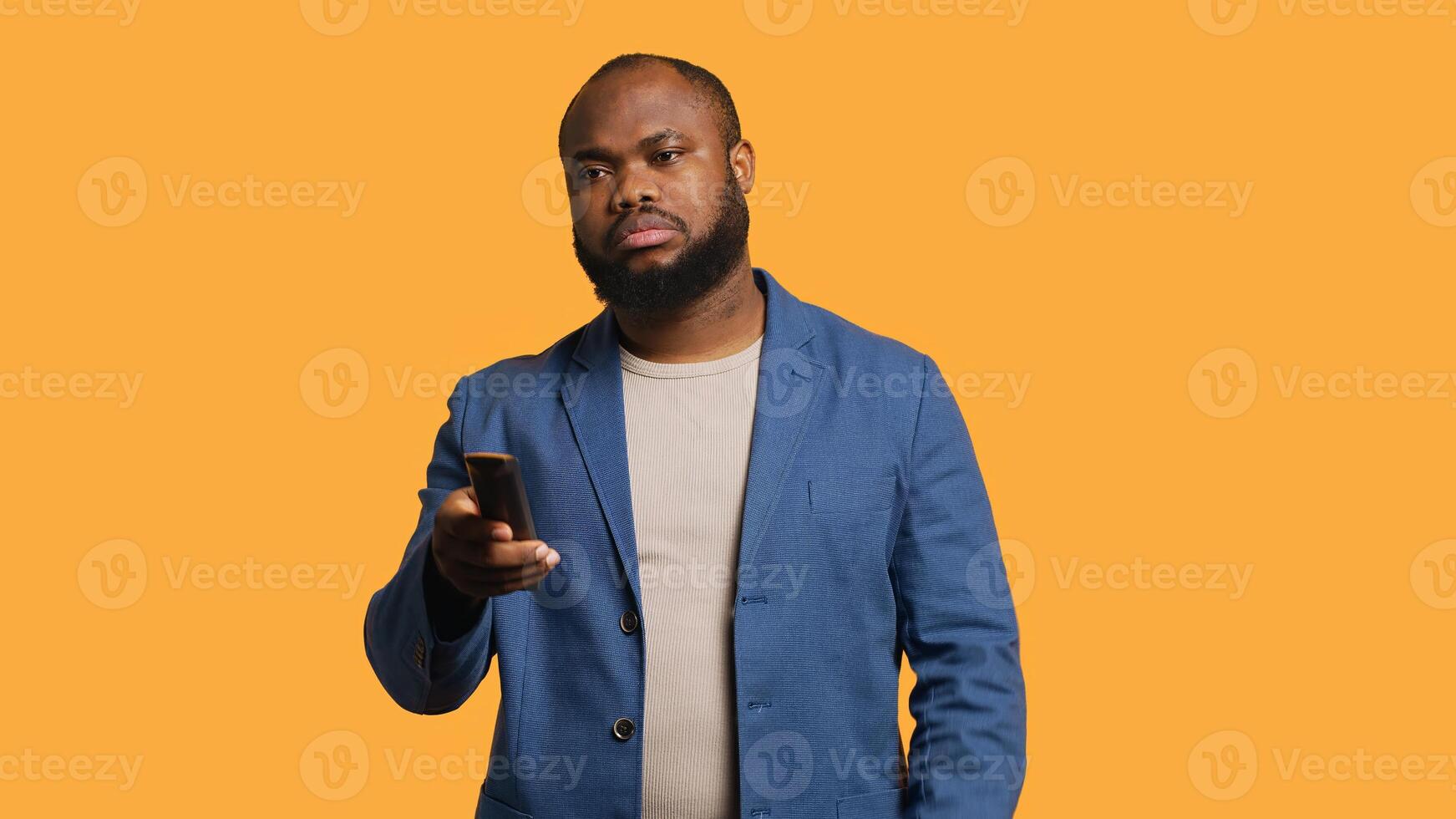 Man zapping through various TV channels, looking for entertaining content to watch, studio background. Person using remote control to select television station, switching between them, camera A photo