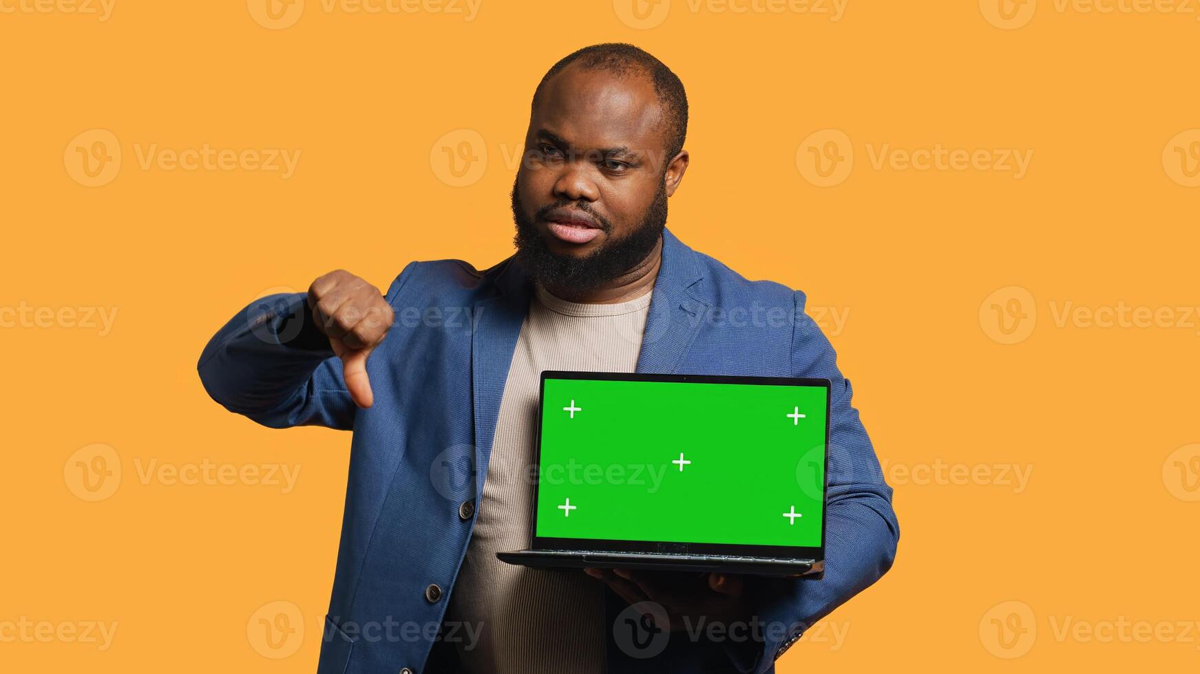 Upset african american man shows thumbs down sign gesturing holding green screen laptop, disapproving. Reviewer does rejection hand gesture regarding chroma key notebook, studio background, camera A photo