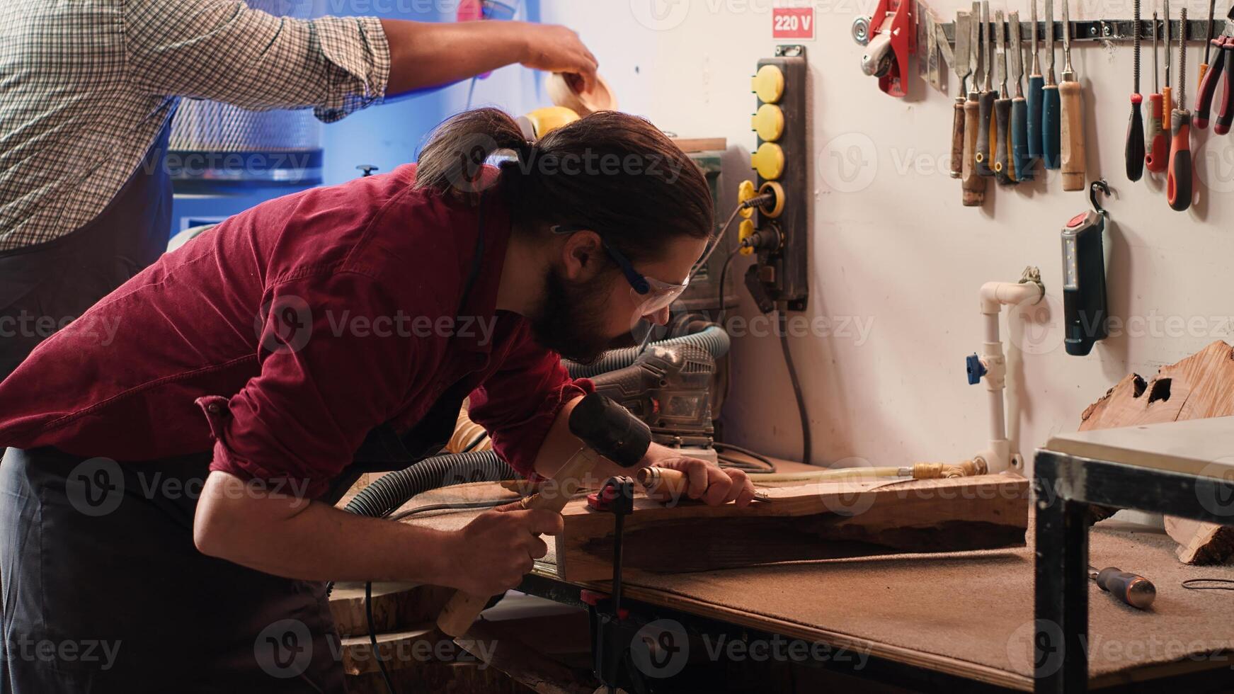 Woodworker using bench vise to hold lumber block, carving intricate designs into wood using chisel and hammer. Craftsperson using vice tool to clamp piece of wood, shaping log with tools, camera A photo