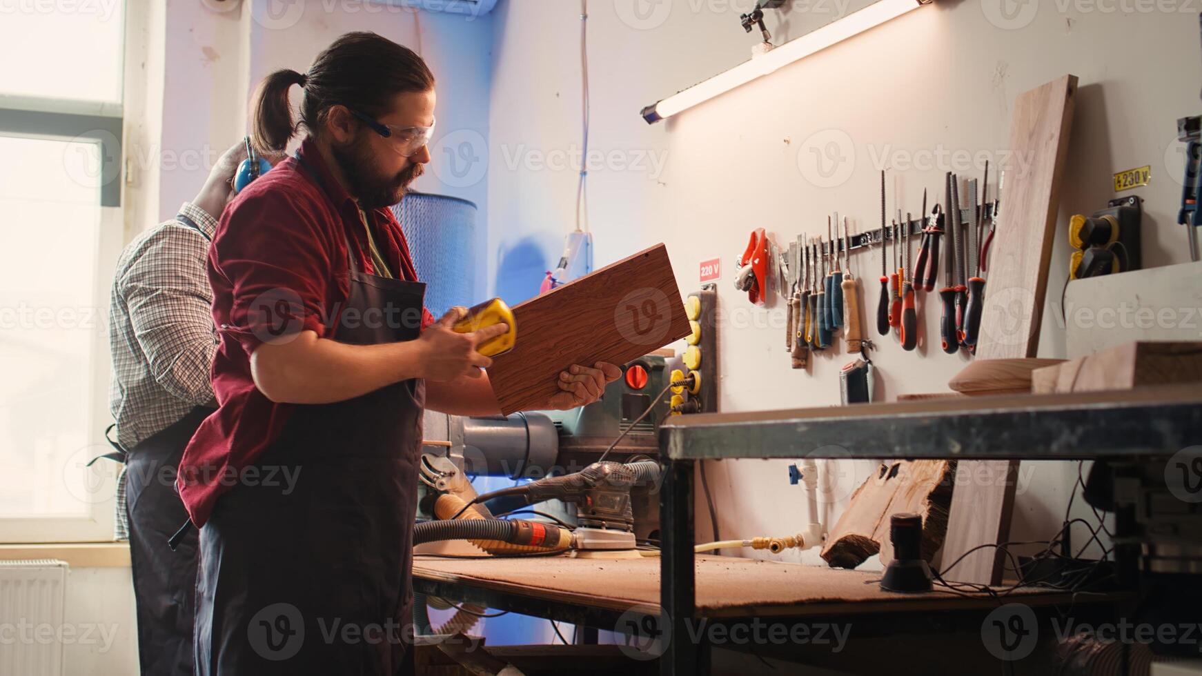 Artisan next to coworker using sanding block to remove imperfections on wood piece. Creative person enjoying diy hobby, using sandpaper to do manual sanding near african american colleague, camera B photo