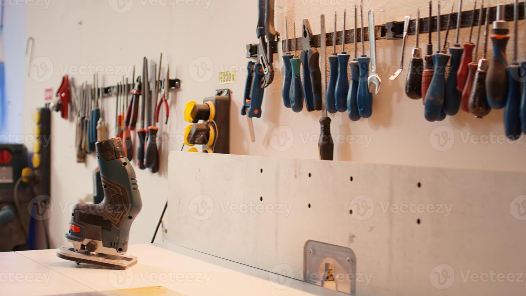 Close up of electric router on workbench in assembly shop with woodworking tools on rack in background. Focus on hand powered gear used for cutting wood in carpentry studio, panning shot photo