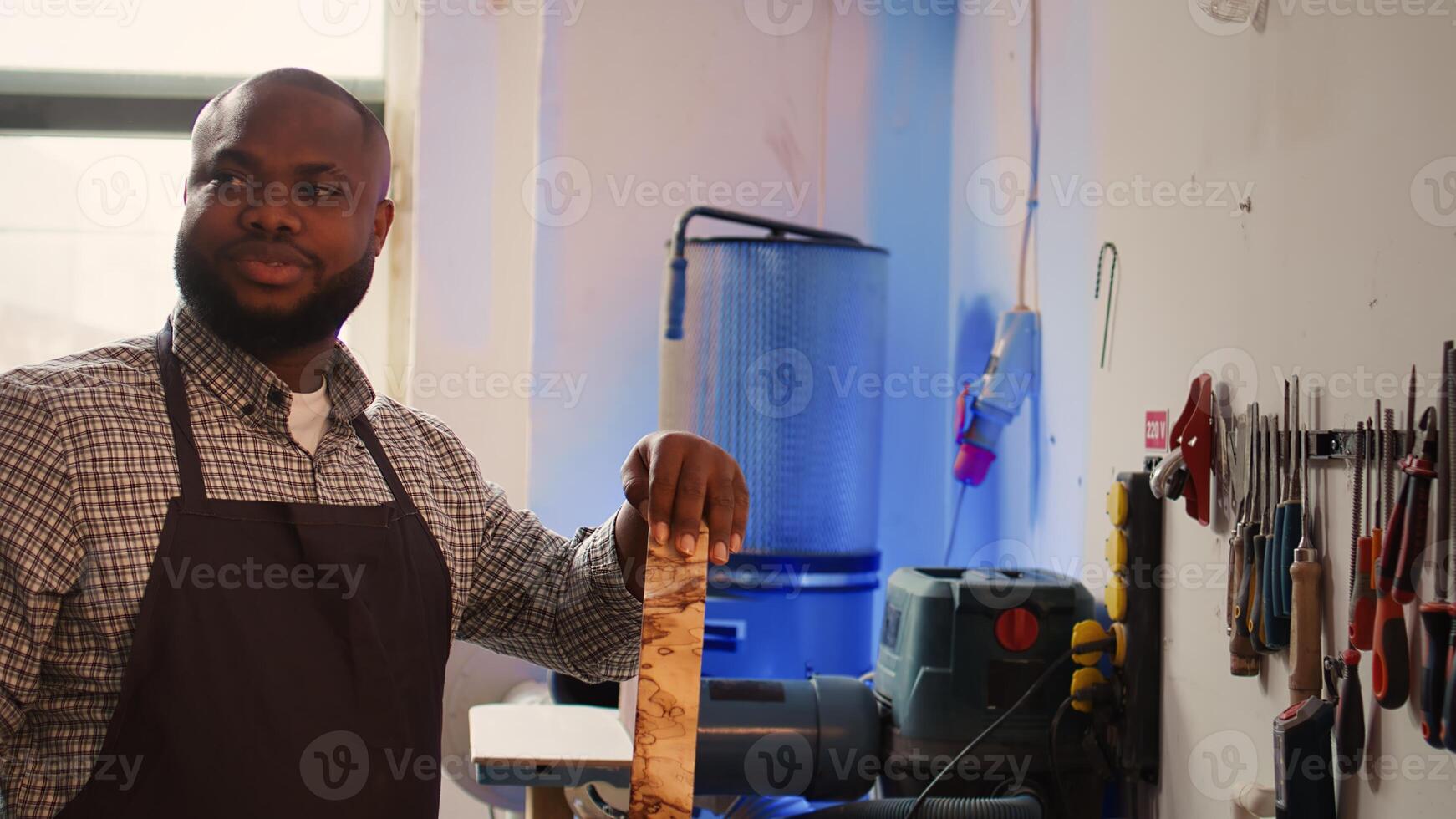 Portrait of jolly man grinning while inspecting wood in furniture assembling shop, satisfied by quality. Joyful woodworking expert in studio evaluates lumber block, pleased by lack of damage, camera B photo