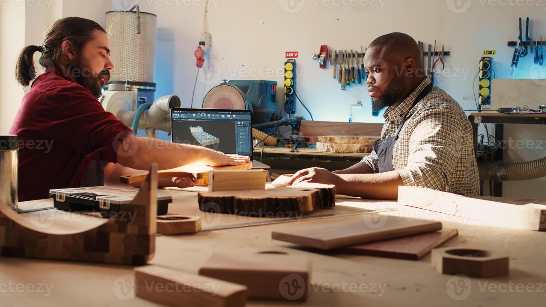 Artisan and apprentice comparing wood art piece with schematic displayed on CAD software on laptop. Woodworking experts in studio crosschecking wooden object with notebook blueprint, camera B photo