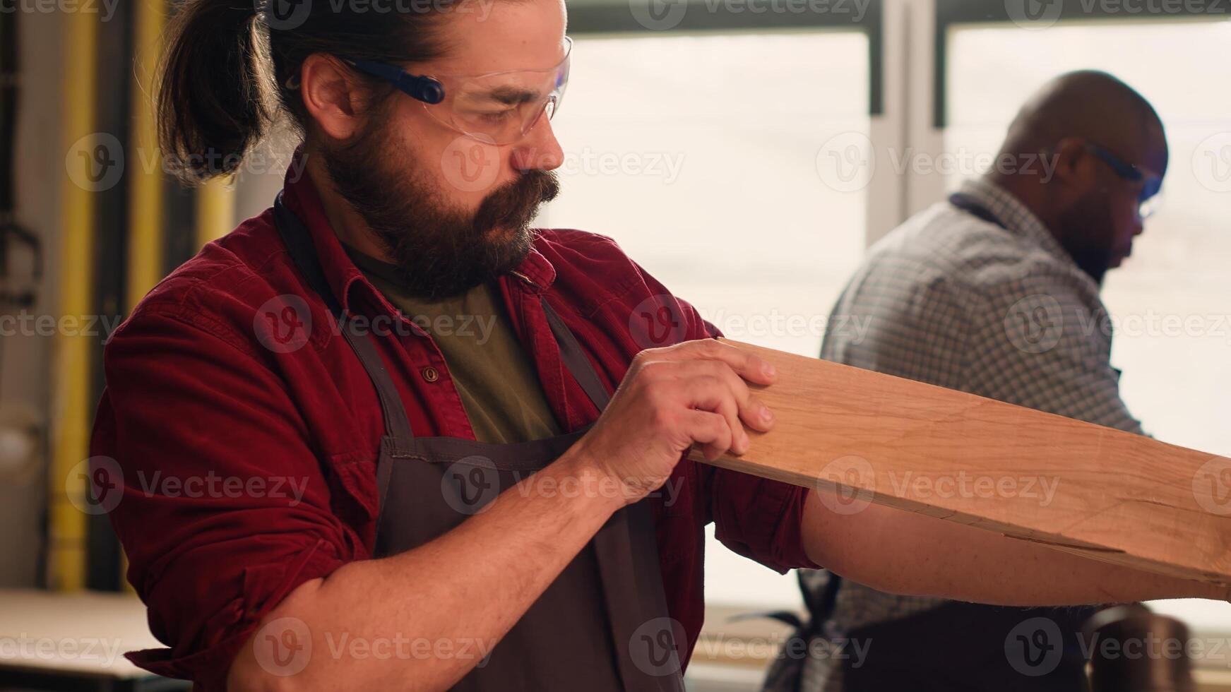 Carpenter putting safety glasses on while selecting quality wood materials meeting project requirements. Cabinetmaker wearing protection gear, doing quality assurance on lumber block, camera A photo