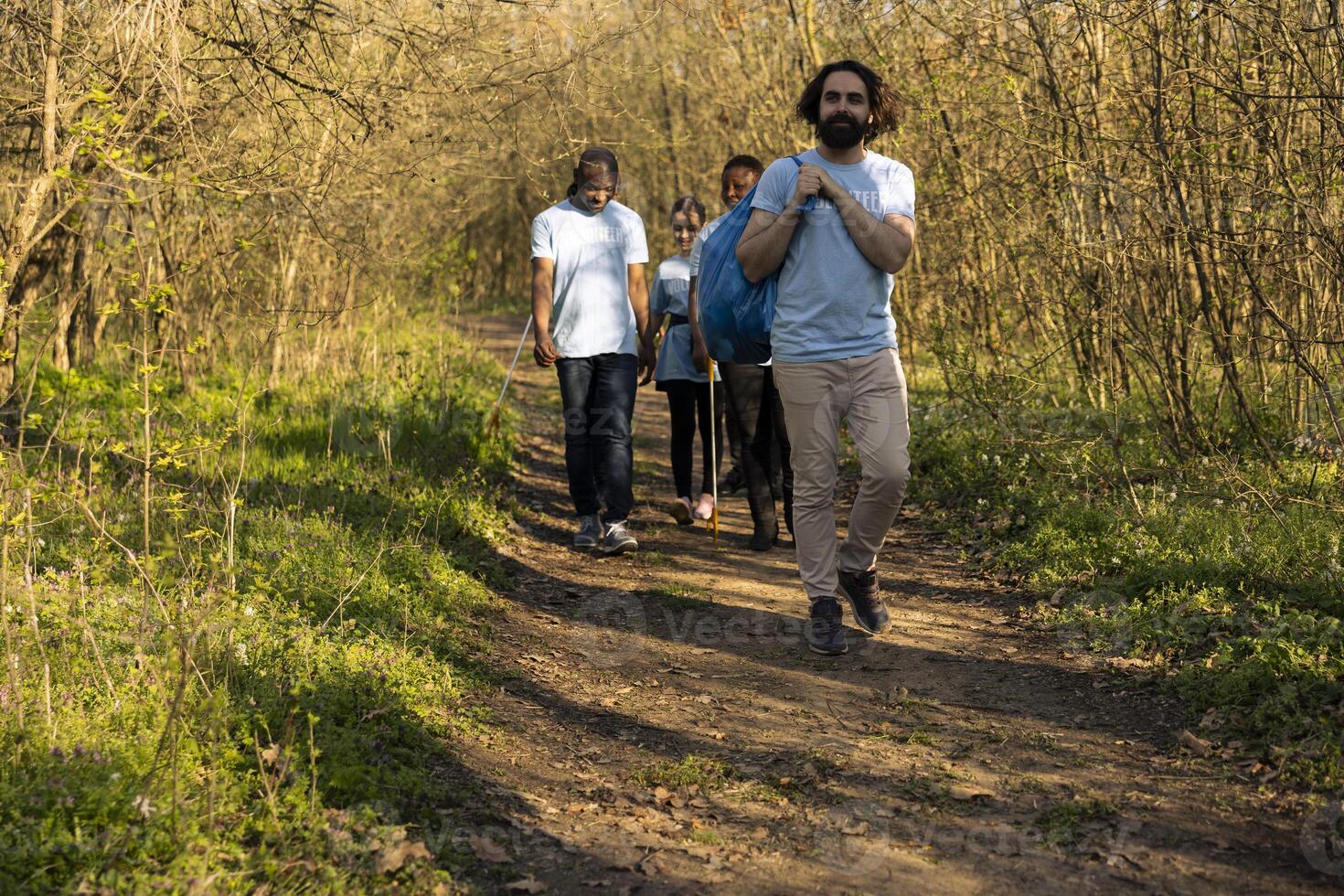 Motivated team of volunteers finishing garbage cleaning mission cleanup in the woods, grabbing their disposal bags and going home. Satisfied people volunteering to clean the ecosystem. photo