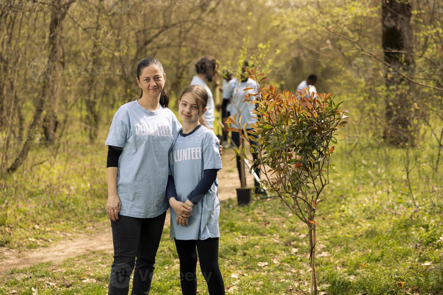 Portrait of mom and her daughter volunteering to plant trees in the forest area, helping with reforestation and conservation of the natural ecosystem. Sense of devotion and responsibility. photo