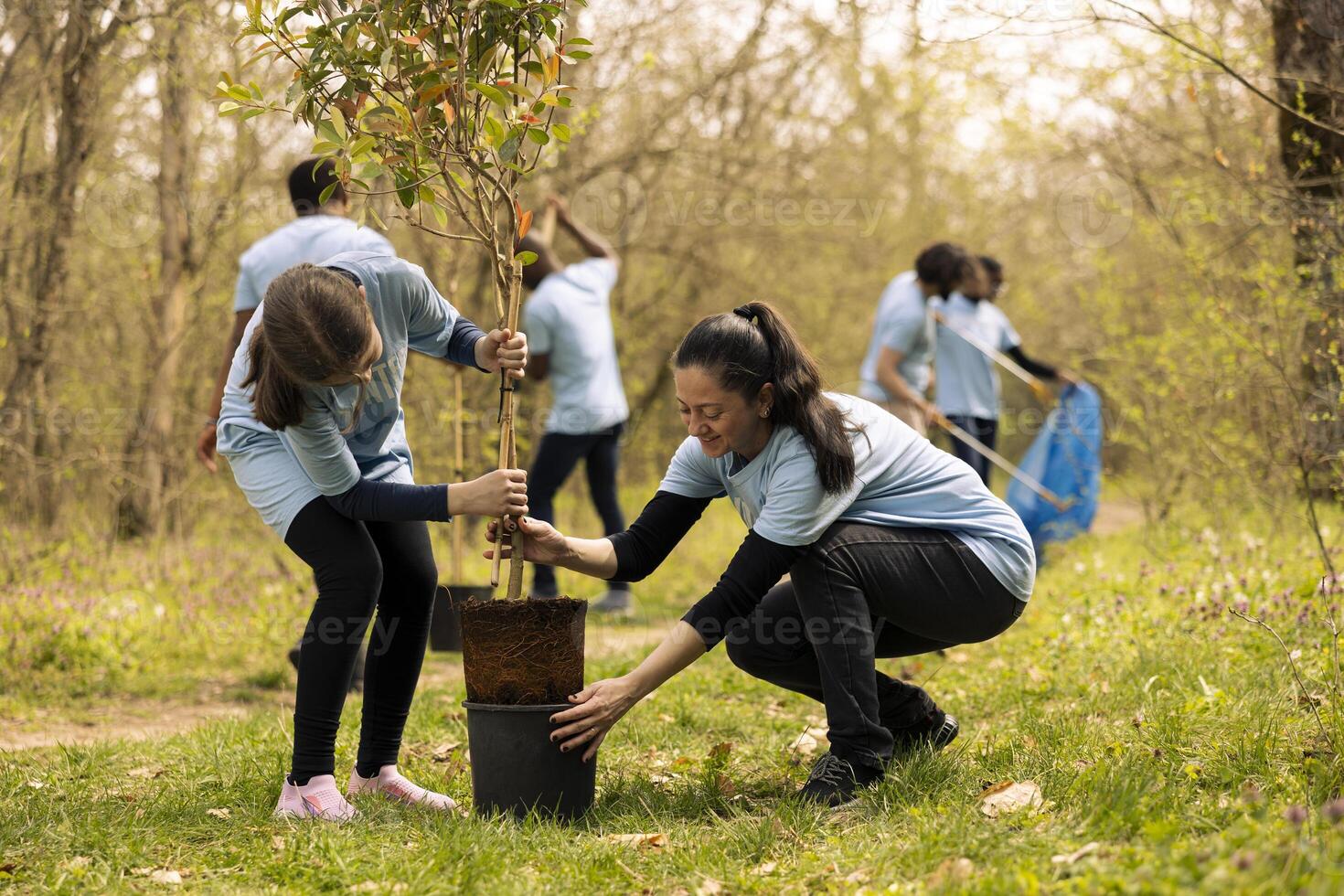 Mom and her little girl taking a tree out of the pot and plant it, doing voluntary work to help with reforestation and environmental protection. Activists taking action to help natural habitat. photo