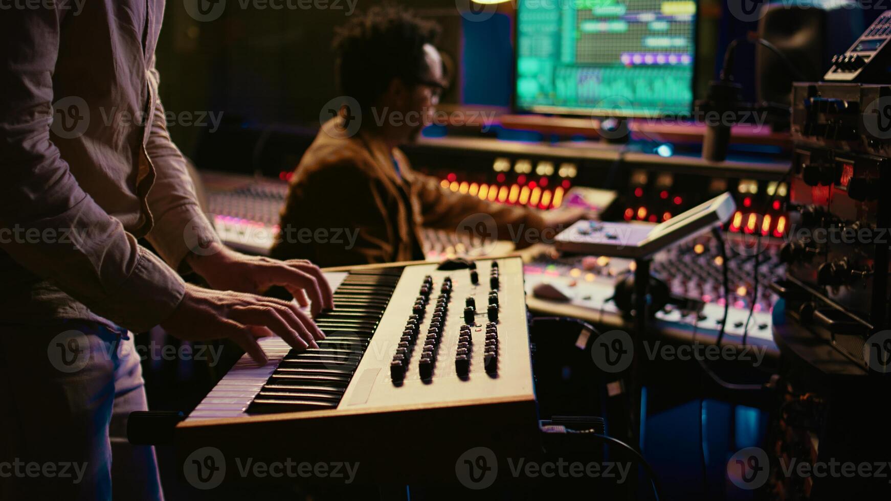 Musician playing piano midi controller in control room at professional recording studio, creating sounds with electronic keyboard notes. Sound engineer does mix and master on files. Camera B. photo