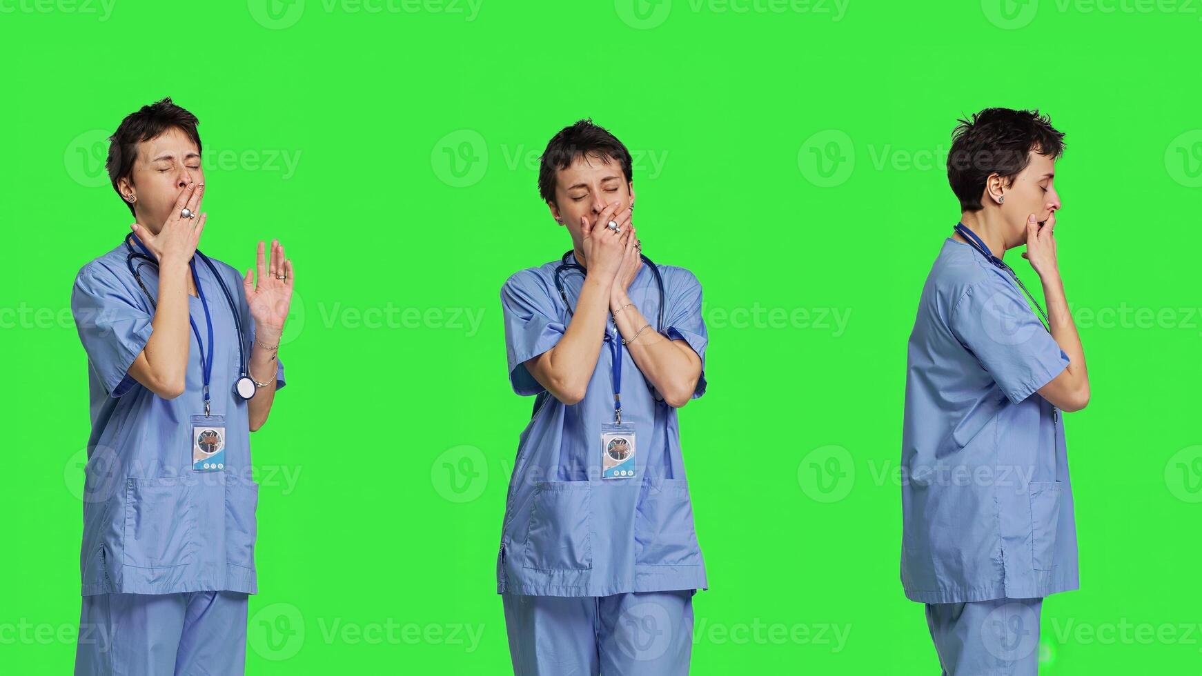 Medical assistant feeling extremely sleepy against greenscreen backdrop, being overworked after the night shift. Woman nurse yawns and feels exhausted in studio, burnout and anxiety. Camera B. photo