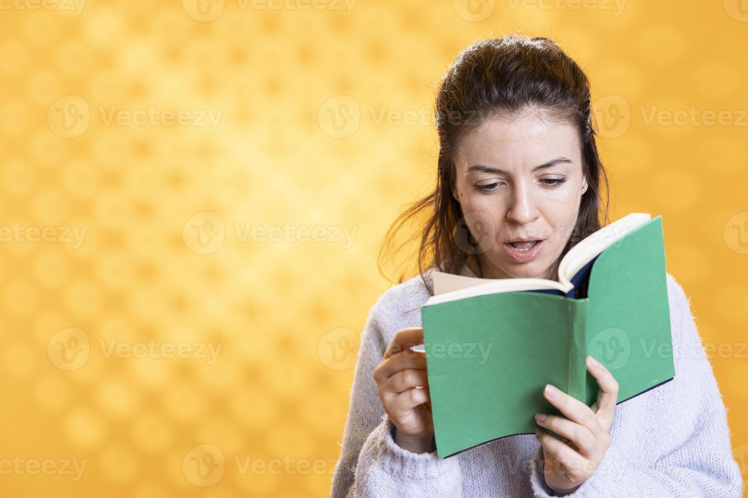 Woman shocked by interesting facts in lecture book needed for school exam, studio background. Student feeling surprised while reading compelling academic textbook needed to pass classes photo