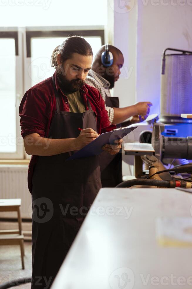 Craftsperson looking over technical drawings of commission on notepad to make creative wood art. Manufacturer looking at blueprints to execute furniture assembling woodworking project photo