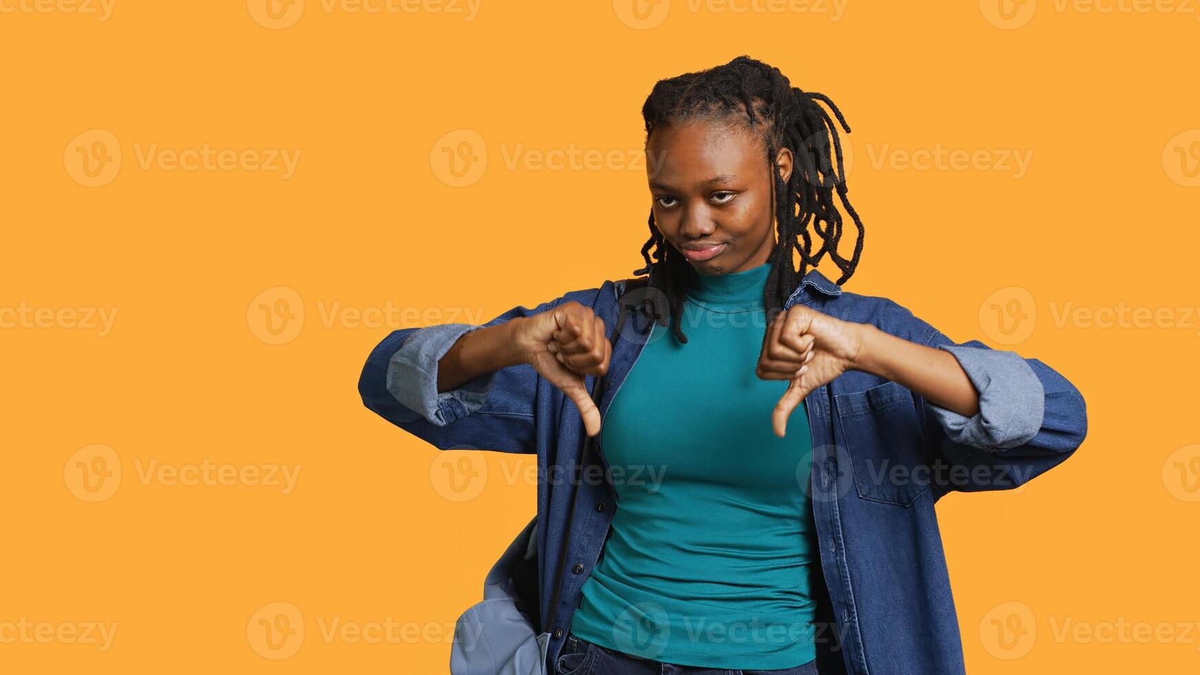 Frustrated woman showing thumbs down sign gesturing, disapproving, offering negative feedback. Disappointed african american girl doing dislike hand gesture, studio background, camera A photo