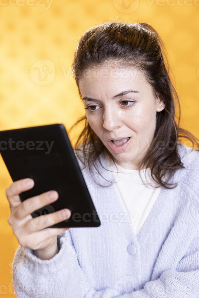 Woman gasping at intriguing ebook on ereader, enjoying hobby during leisure time. Person with tablet in hands shocked by digital novel plot twists, isolated over studio background photo