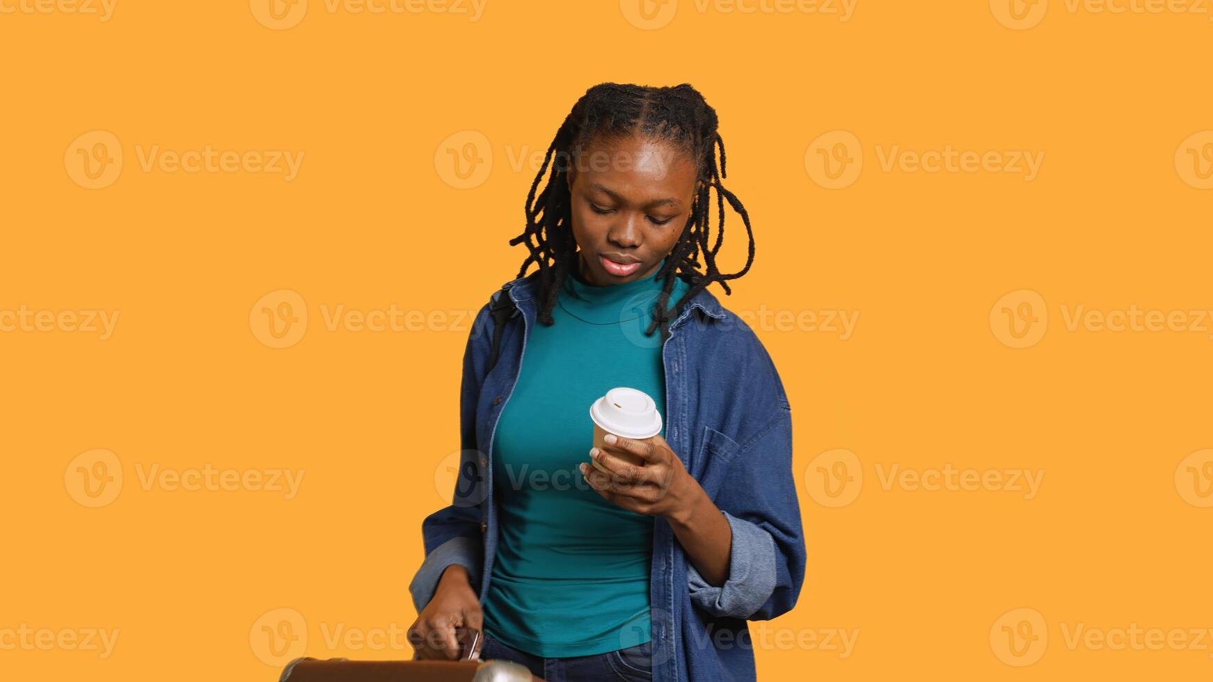 Tired girl travelling with suitcase, drinking coffee to wake up. Sleepy woman using caffeinated beverage to gain energy, going abroad with briefcase, studio background, camera A photo