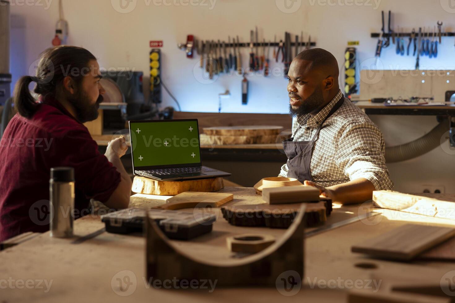 Woodworker looking over blueprints on green screen laptop in CAD software with apprentice. Manufacturer and coworker designing custom 3D furniture on chroma key notebook in studio photo