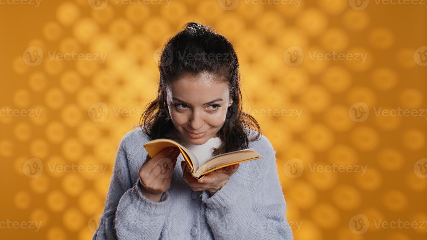 Portrait of smiling woman holding book smelling pages conveying joy of reading concept, studio background. Cheerful person liking new novel fresh smell, showing blissfulness, camera B photo