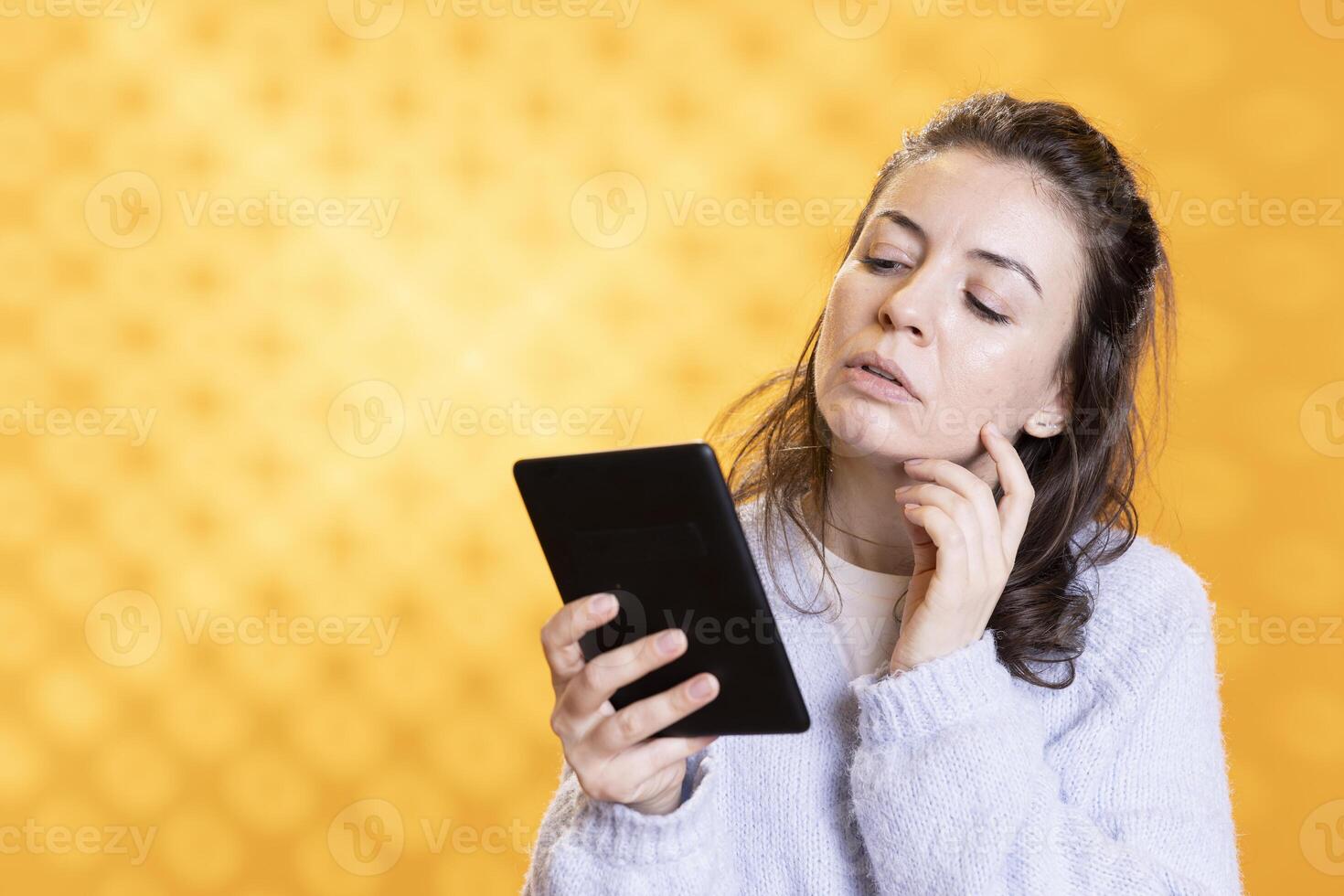 Woman reading textbooks on electronic ebook reader, gathering information for school exam, isolated over studio background. Student looking at digital books on tablet device display photo