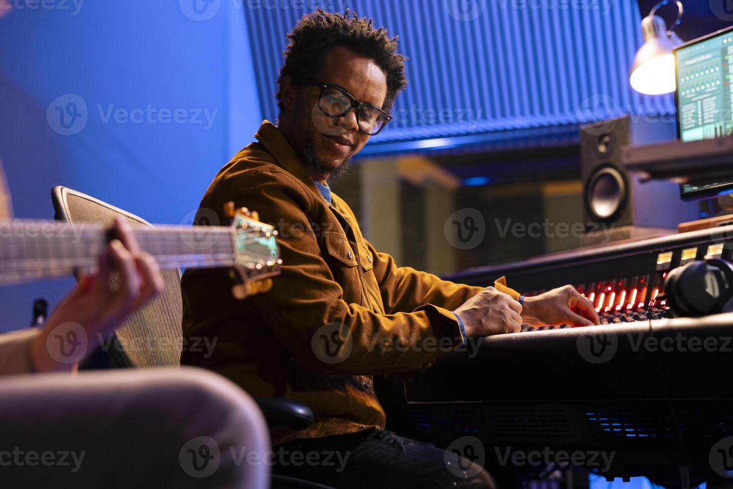 Musician creating a new hit song with guitar in control room, recording electro acoustic instrument accords in professional studio. Artist performing live next to his sound designer, edit tracks. photo