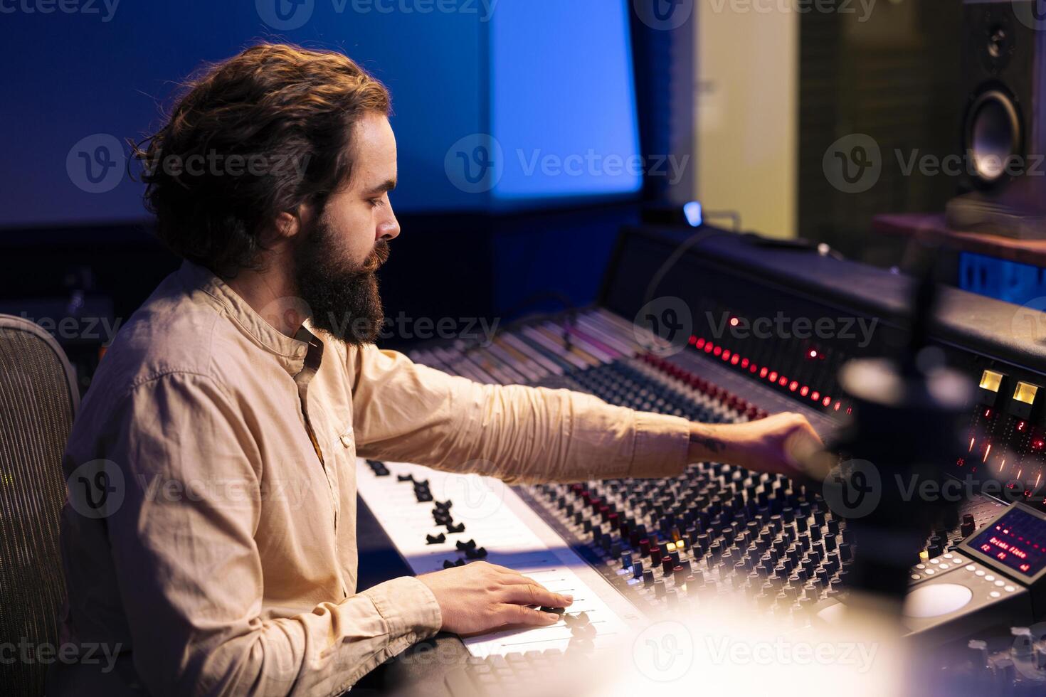 Music producer editing and mixing tunes in control room, working on a new song in professional recording studio. Audio engineer using control panel board with buttons and motorized faders. photo