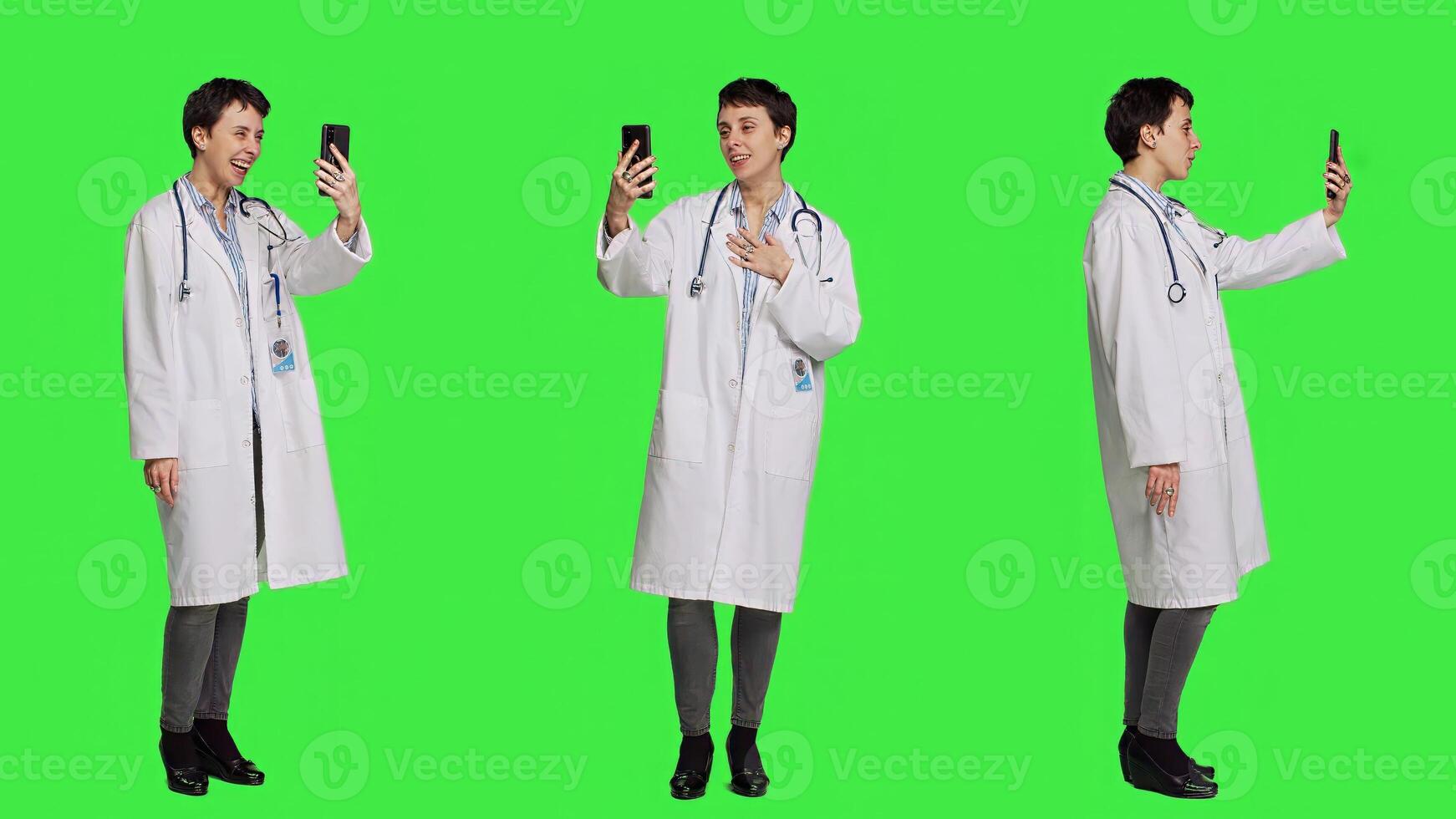 Medic specialist having remote videocall conversation with patients on smartphone internet connection, greenscreen backdrop. Doctor discusses about disease with people on videoconference. Camera A. photo