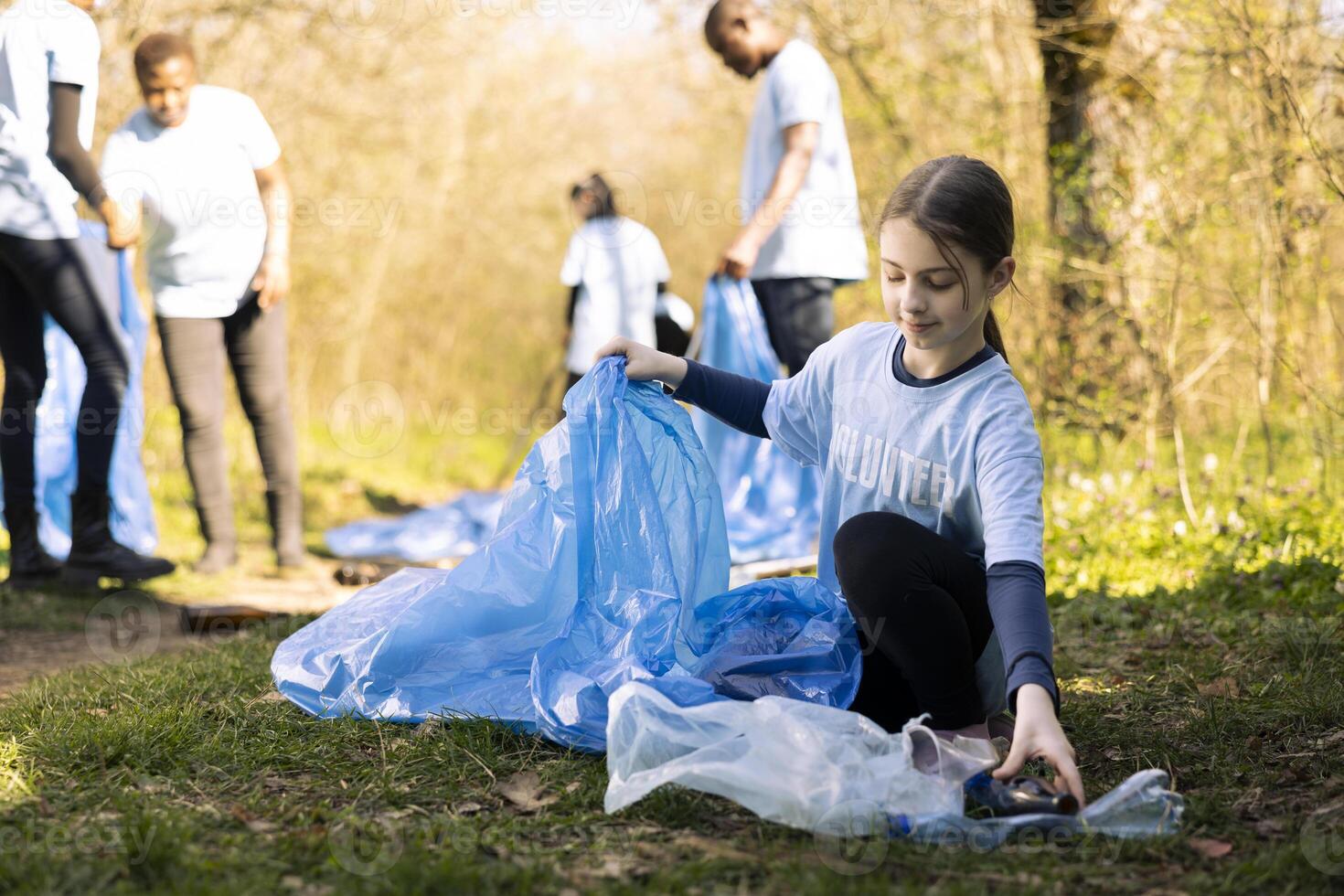 Young girl activist collecting trash and recycling in disposal bags, clearing the natural forest environment and combating illegal dumping. Ecologic volunteer grabbing plastic waste and junk. photo