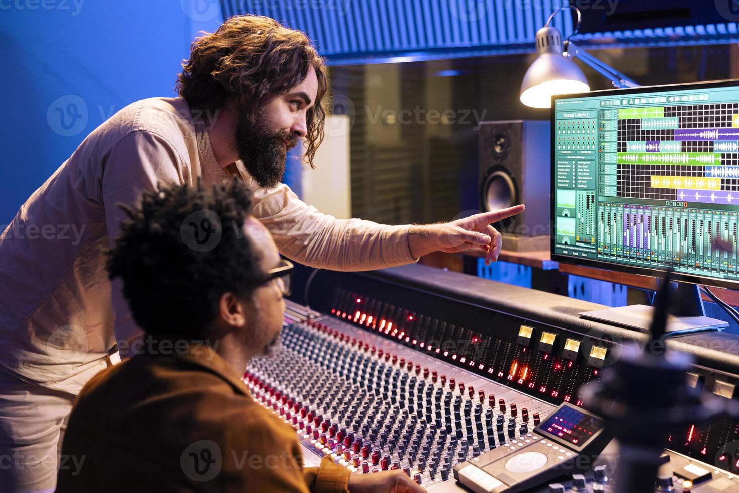 Young performer working on new album with his record producer in studio, processing sounds and mixing them in post production. Musician collaborating with audio expert to edit recorded music. photo