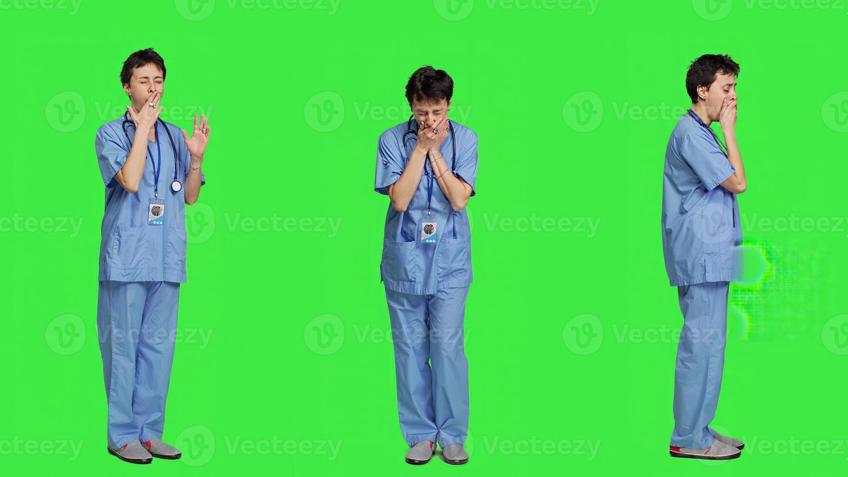 Medical assistant feeling extremely sleepy against greenscreen backdrop, being overworked after the night shift. Woman nurse yawns and feels exhausted in studio, burnout and anxiety. Camera A. photo