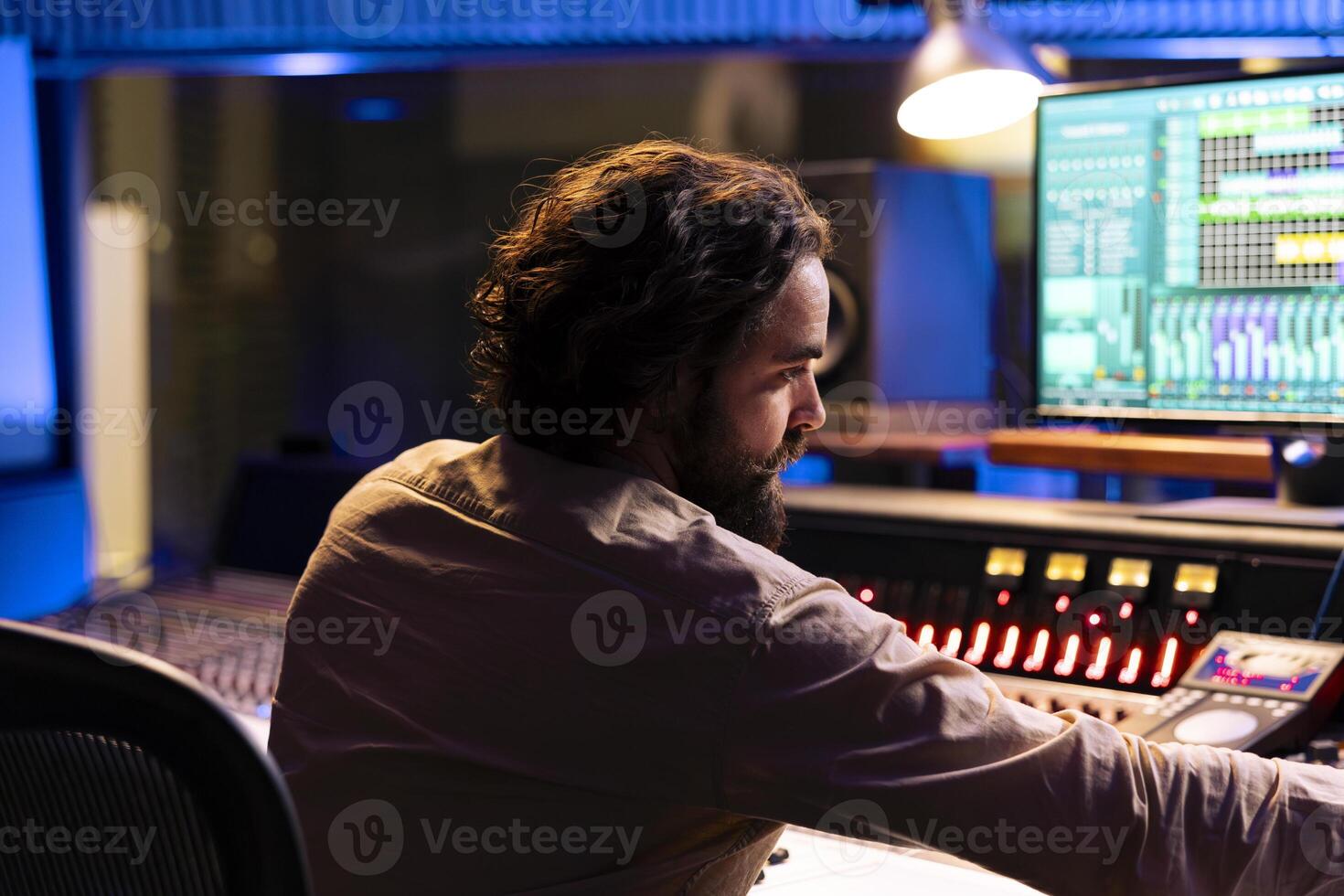Sound technician producing new music with mixing console, editing tunes with digital software on computer. Skilled music producer processing sounds in control room, uses panel board. photo