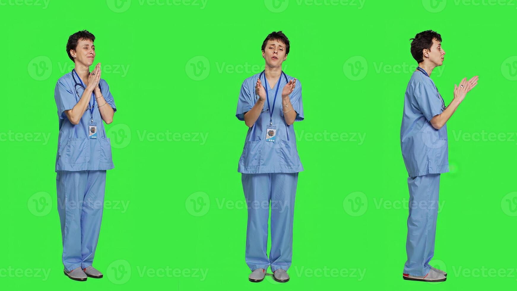 Smiling medical assistant applauding someone in studio, celebrating success and cheering against greenscreen backdrop. Young nurse clapping hands and feeling happy about achievement. Camera A. photo