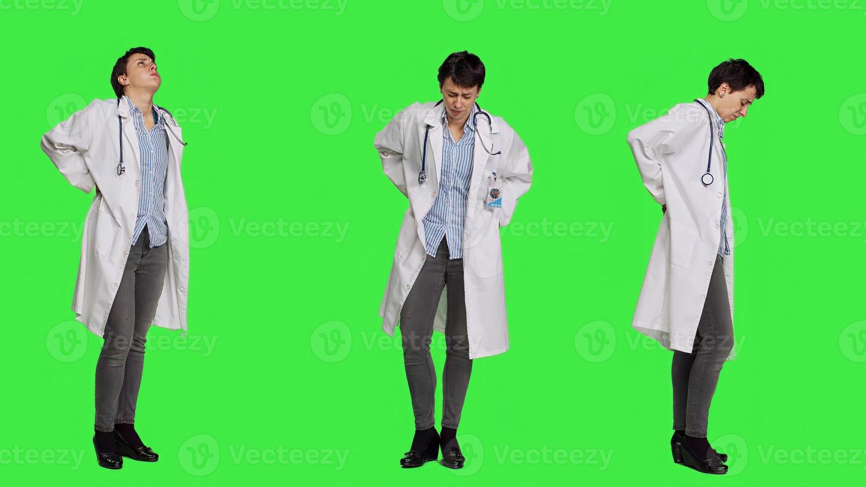 Woman physician experiencing lower back acute pain in studio, suffering from scoliosis and having muscles discomfort. Medic dealing with backache from burnout, greenscreen backdrop. Camera A. photo