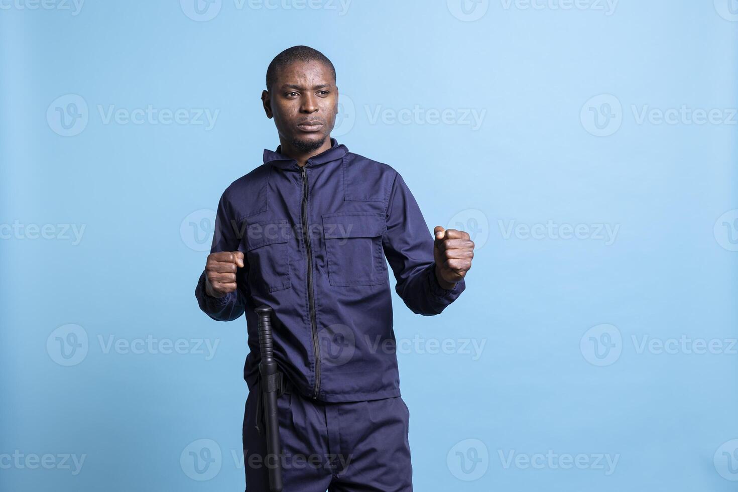 Serious african american guard clenching his fists in front of camera, preparing for a fight to protect and defense a property. Armed bodyguard with good combat protection training. photo