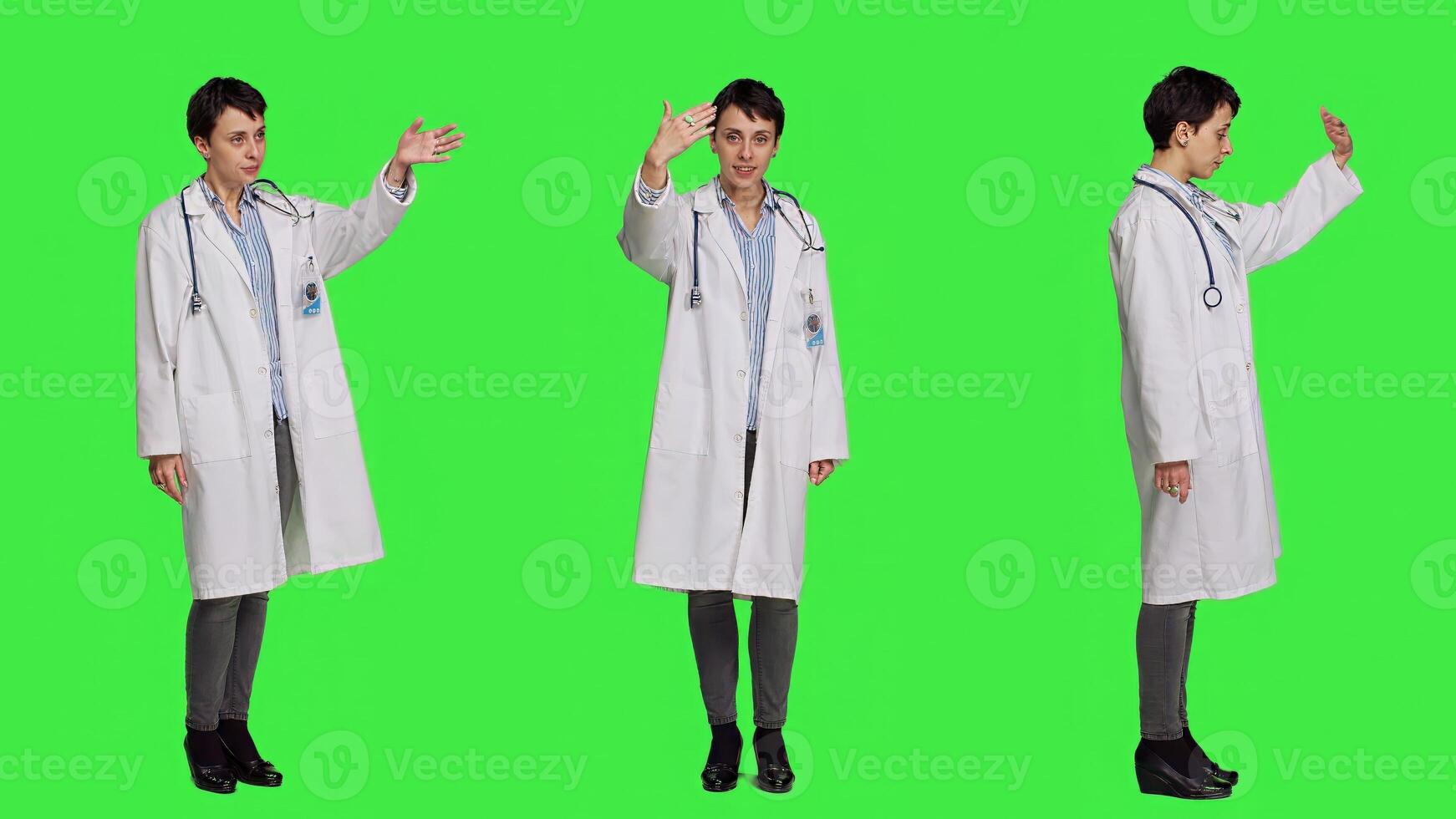 Friendly physician inviting people to come closer to her against greenscreen backdrop, calling patients over and smiling. General practitioner asking persons to approach her. Camera A. photo
