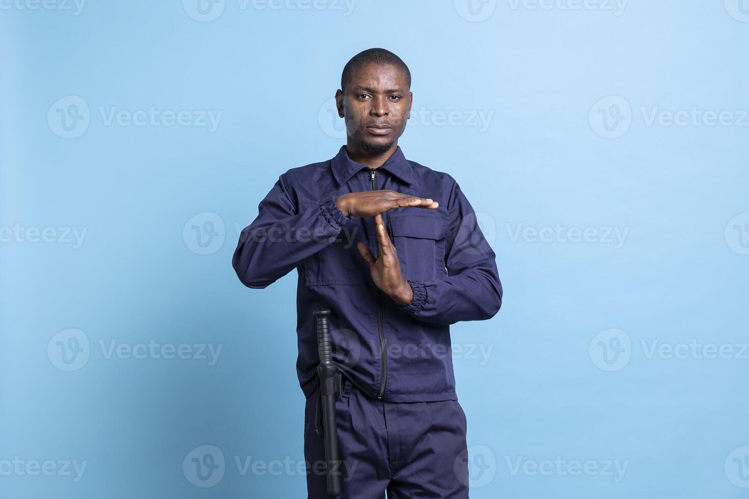 Patrol officer presenting a timeout symbol against blue background, asking for a break while he is on safeguard duty. Man in bodyguard uniform showing a pause sign, needs to relax. photo
