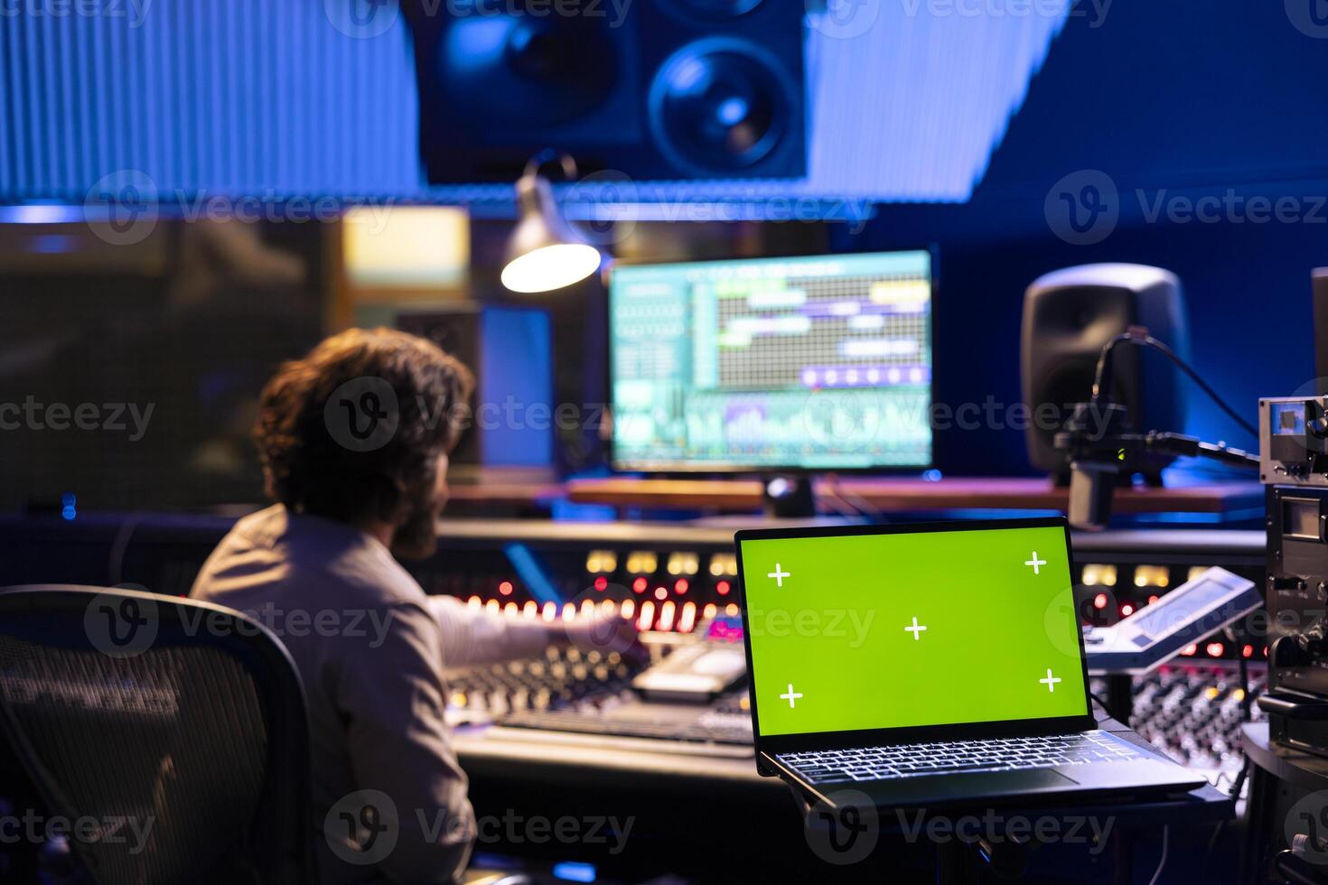 Sound engineer working on control desk with greenscreen layout in professional studio, using sliders and knobs to edit music for album. Audio technician operates soundboard panel for tracks. photo