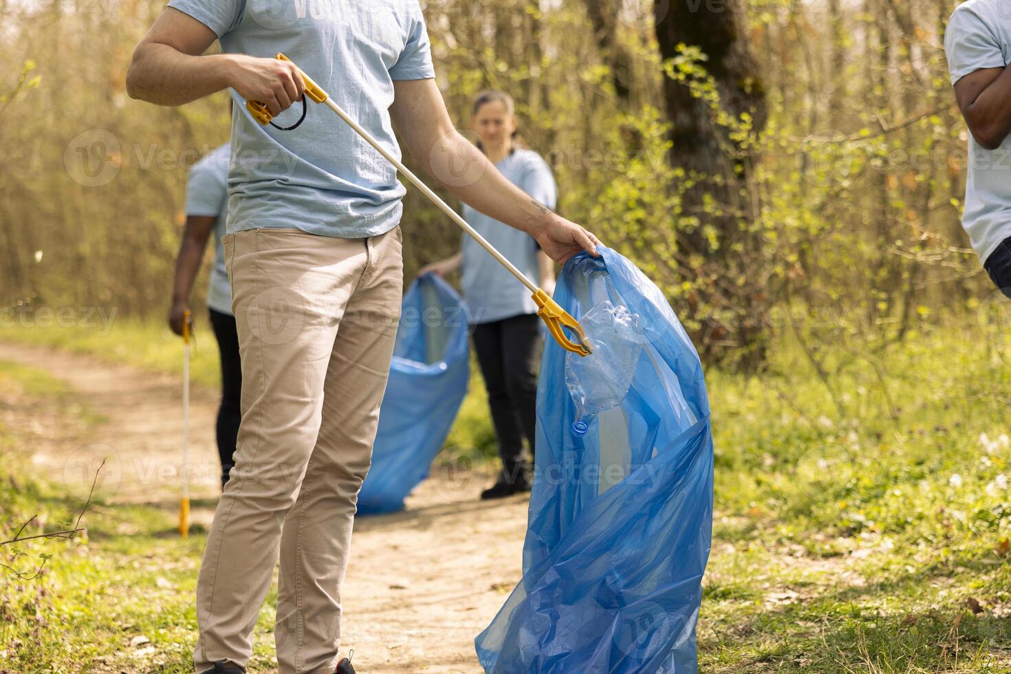 Male volunteer collecting rubbish to fix pollution issues within the habitat, protecting the natural ecosystem. Activist doing voluntary work to clean the woods from trash and plastic waste. photo