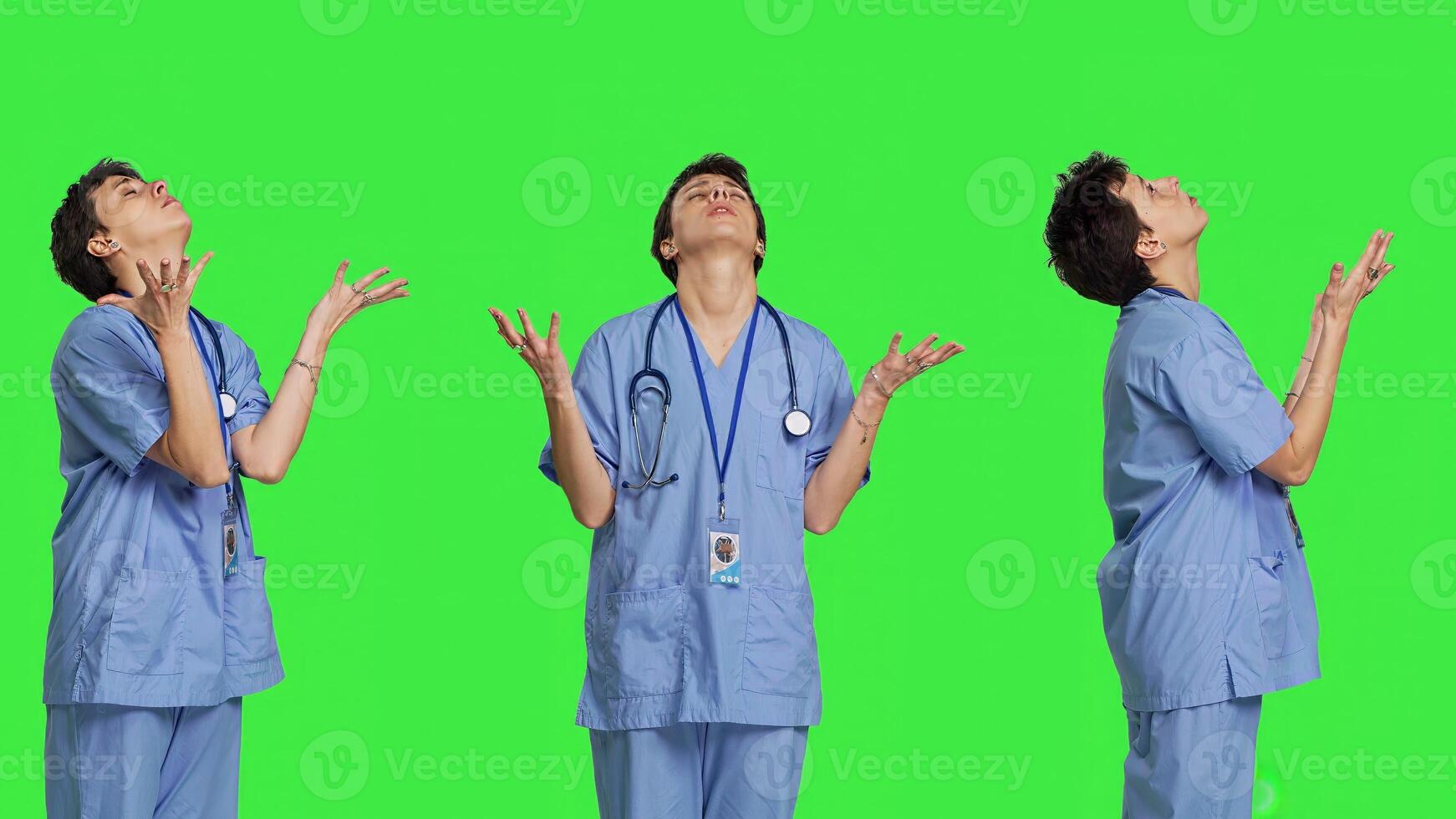 Hospital nurse worshipping God by prayer against greenscreen backdrop, praying to jesus christ and having hope in christianity and spirituality. Medical assistant doing meditation. Camera B. photo