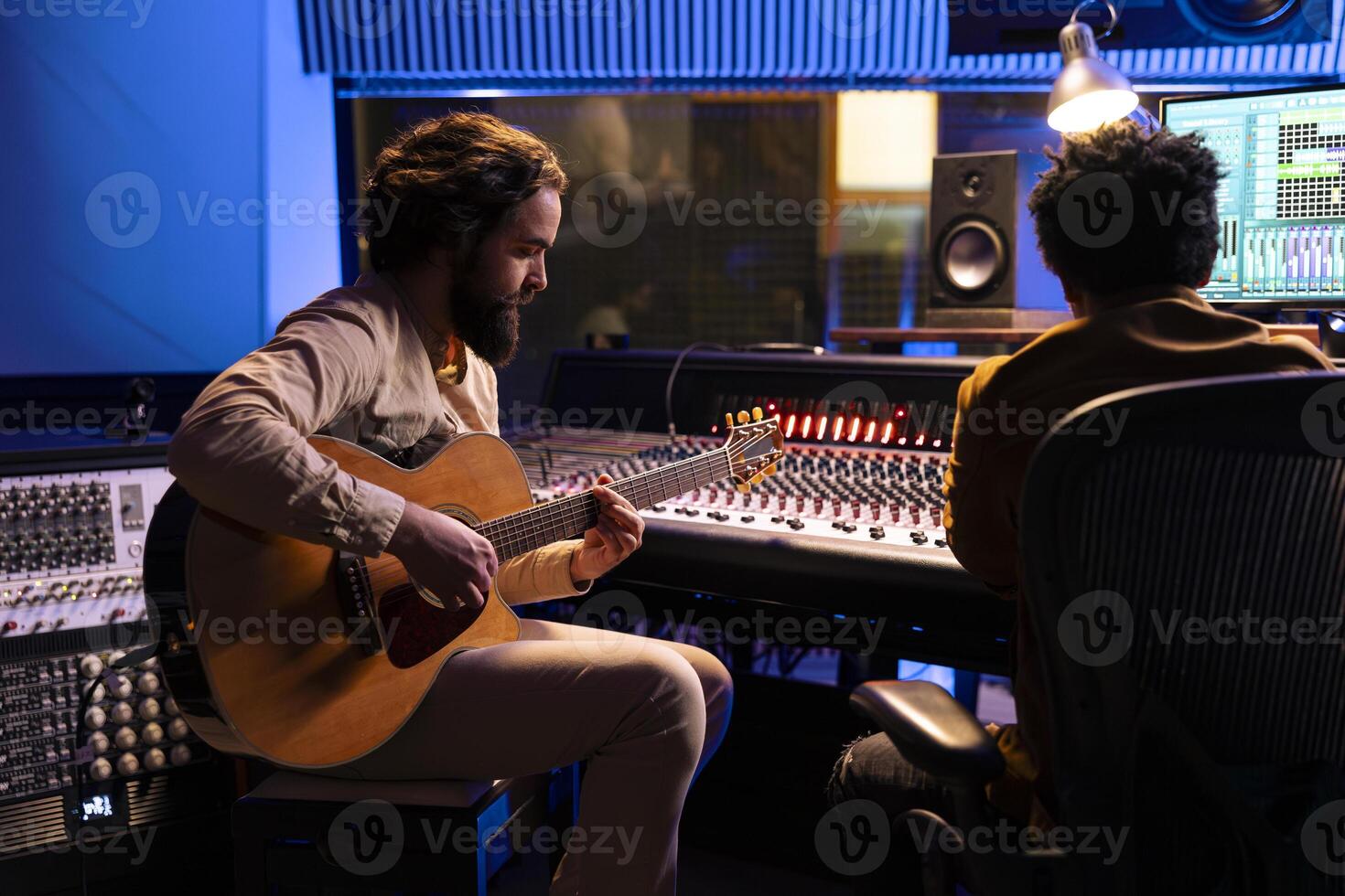 Singer creating a new hit song in studio with guitar running, working with audio expert to produce music. Songwriter singing a record on electro acoustic instrument in control room with soundboard. photo