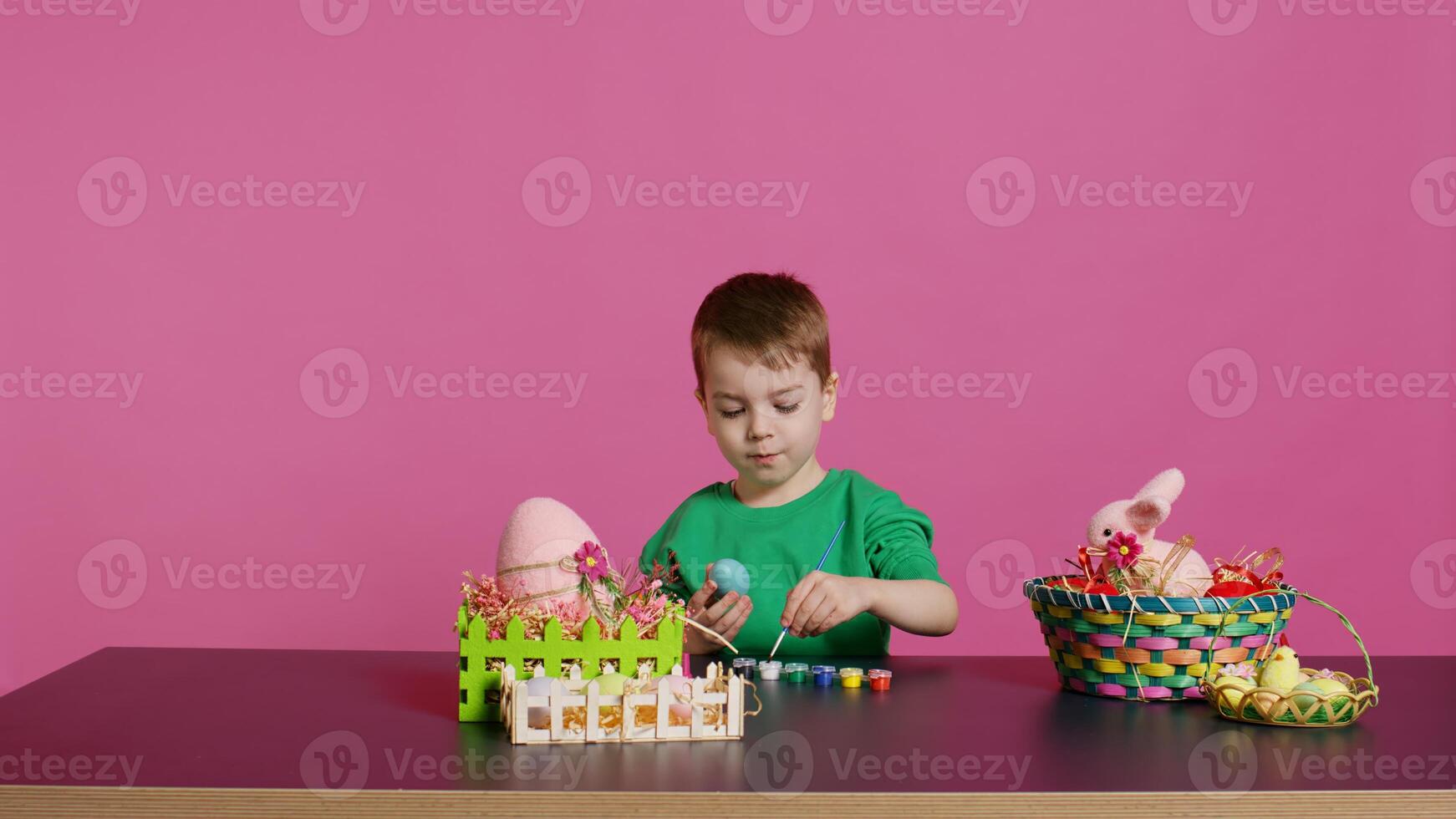 Joyful small kid painting eggs for easter holiday festivity in studio, using watercolor and art supplies. Smiling preschooler coloring festive ornaments in preparation for sunday. Camera B. photo
