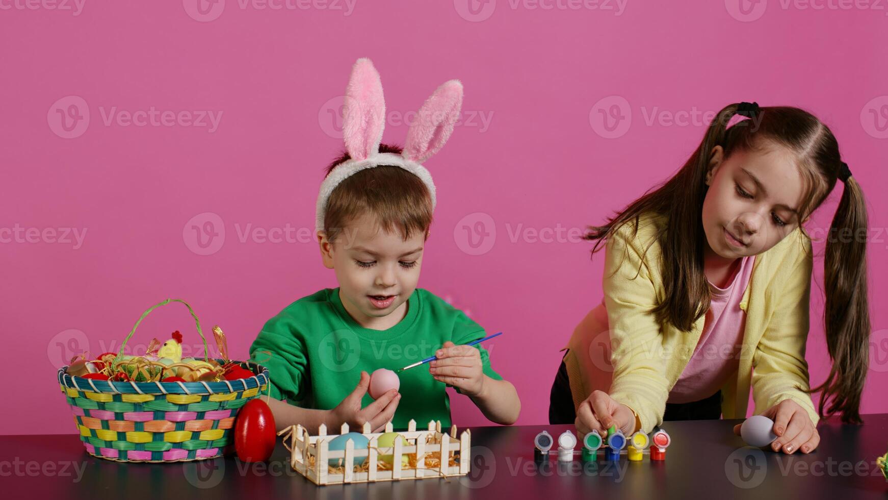 Young adorable kids coloring easter eggs with watercolor paint, creating lovely designs to celebrate spring holiday. Cheerful brother and sister painting festive decorations in studio. Camera B. photo
