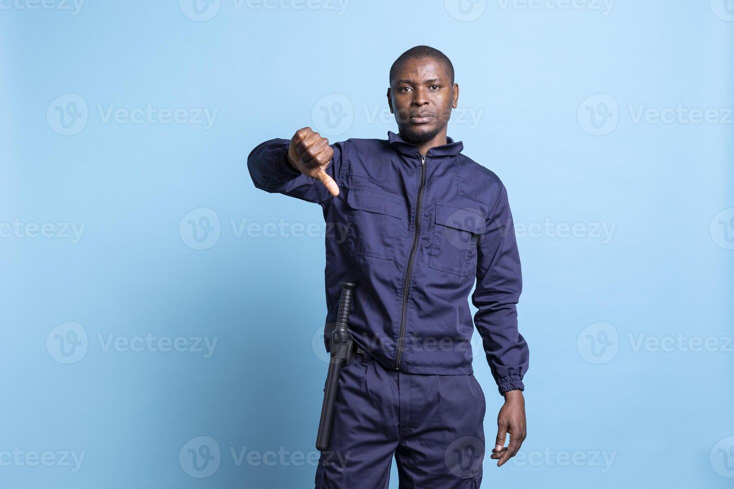Security guard showing thumbs down negative symbol in front of the camera, presenting his disapproval about an idea. Agent shows his authority by denying a thing, dislike gesture in studio. photo