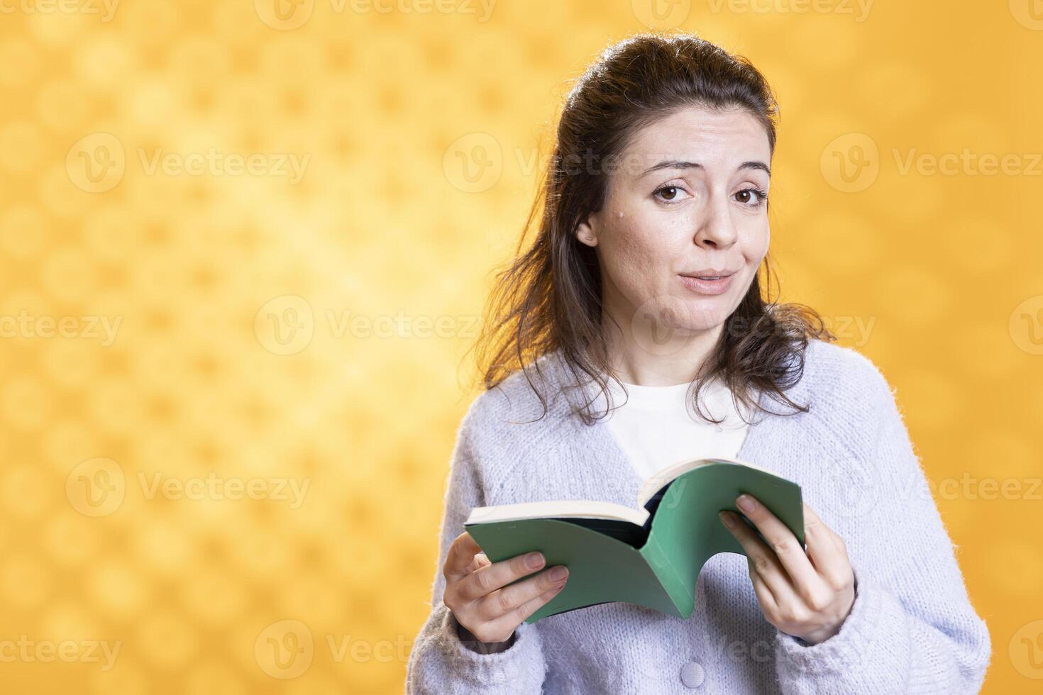 Portrait of smiling woman focusing on gathering information from book for school exam, isolated over studio background. Relaxed upbeat student reading textbook for university assessment photo