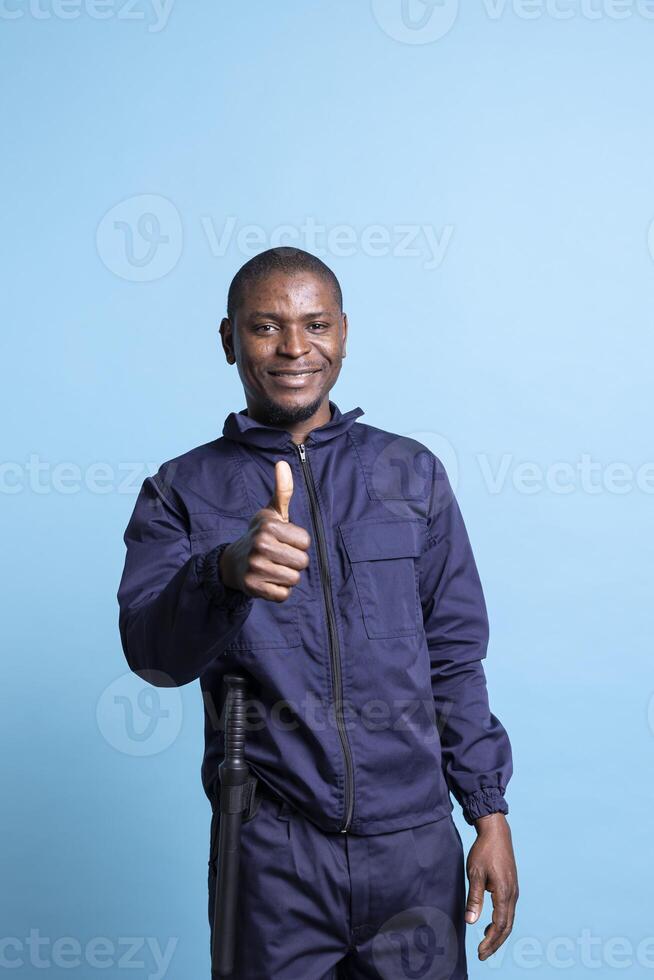 Happy optimistic security guard giving a thumbs up sign on camera, spreading positivity and showing a like symbol. Smiling confident african american bodyguard doing approval gesture. photo