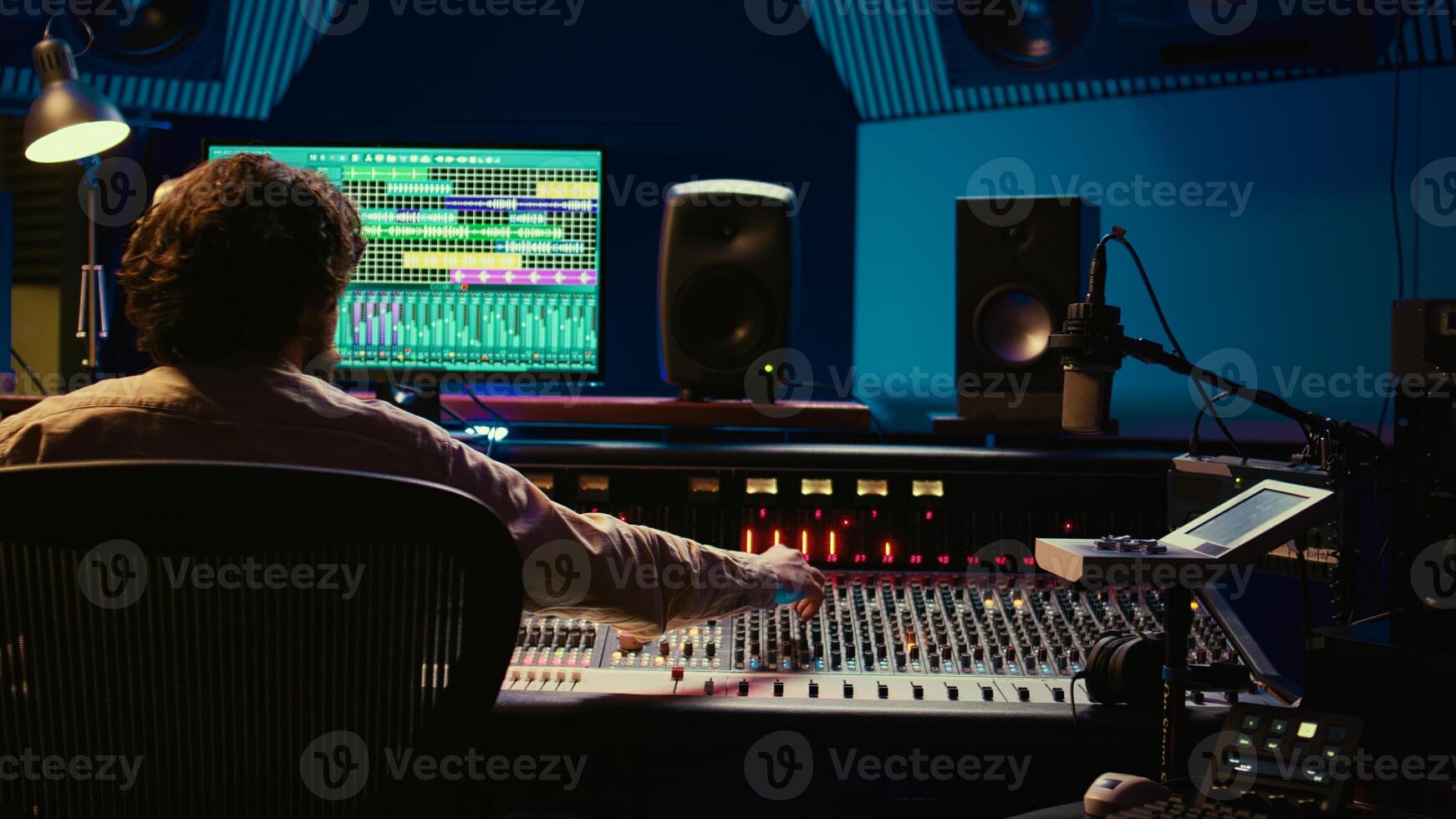 Tracking engineer processing and mixing sound on audio console with moving faders and colored meters. Music producer working on a new album, creating a hit song in studio. Camera B. photo