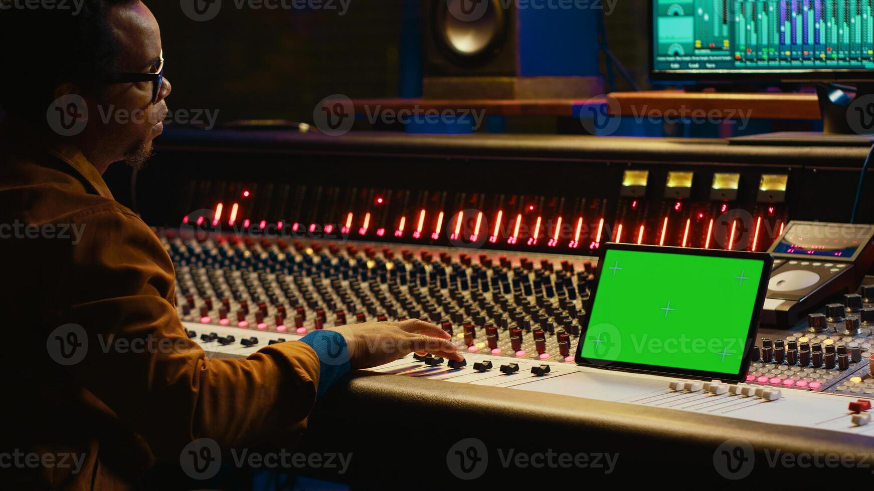 Professional audio technician recording tracks with mockup on tablet, creating tunes on mixing console to add on songs in post production. Engineer pressing buttons, process sounds. Camera A. photo