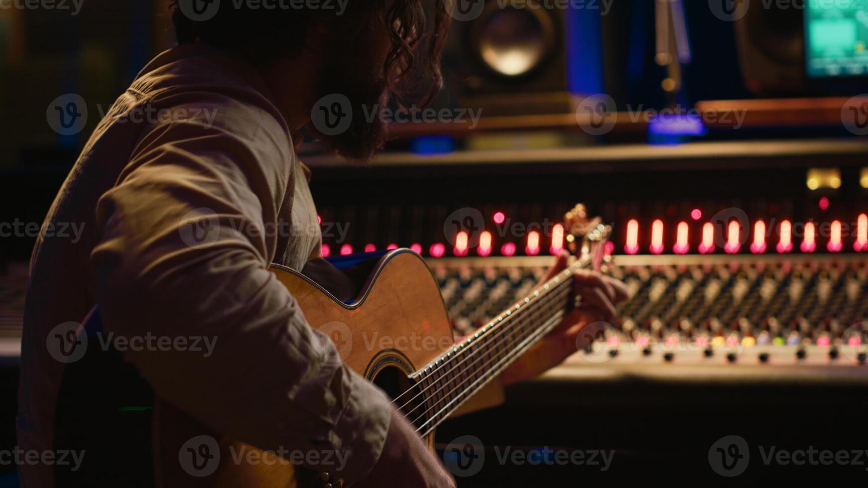 Songwriter composing a song with sound engineer in professional studio, recording session with his electro acoustic guitar in control room. Musician producing tracks with mixing console. Camera A. photo