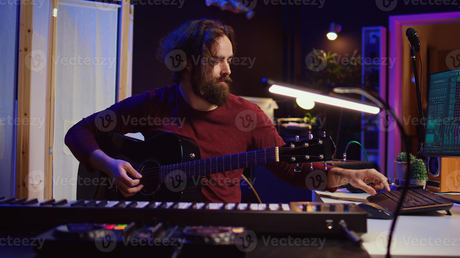 Artist working with daw software at his home studio to record new music on mixing console and soundboard, audio engineering. Musician playing song on guitar and adjusting volume. Camera B. photo
