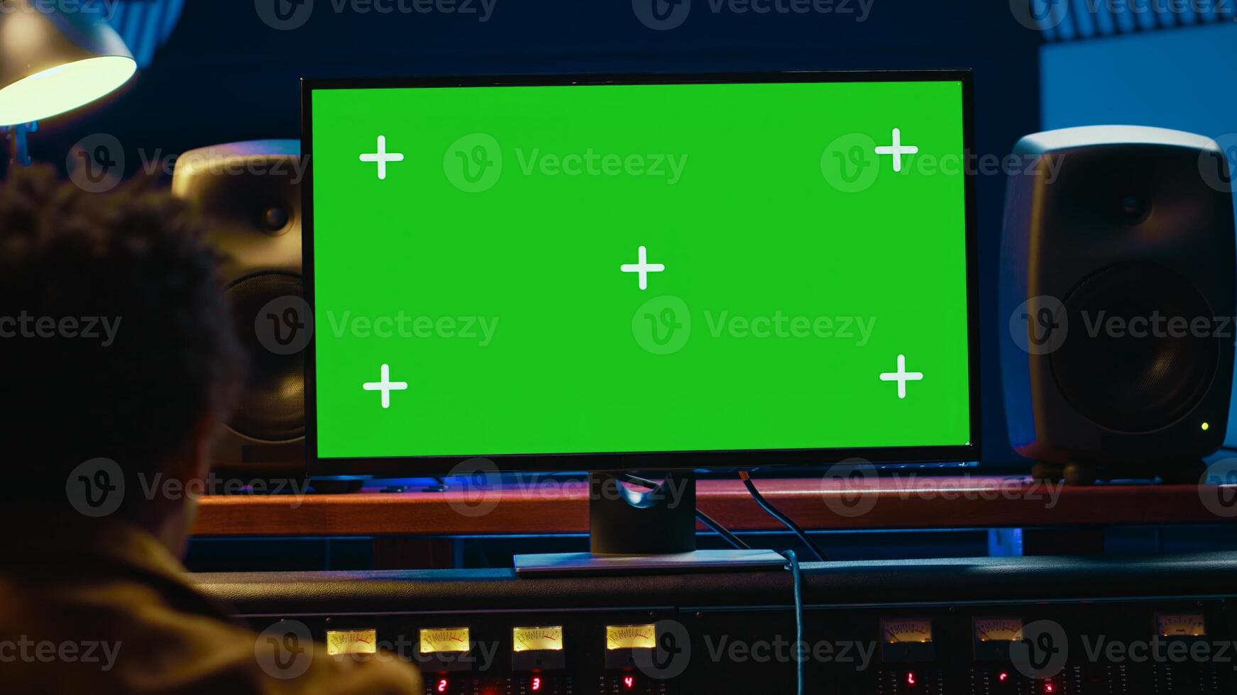African american audio engineer uses greenscreen on pc in professional recording studio, working with mixing console and twisting knobs to edit tracks. Music producer creating tunes. Camera A. photo