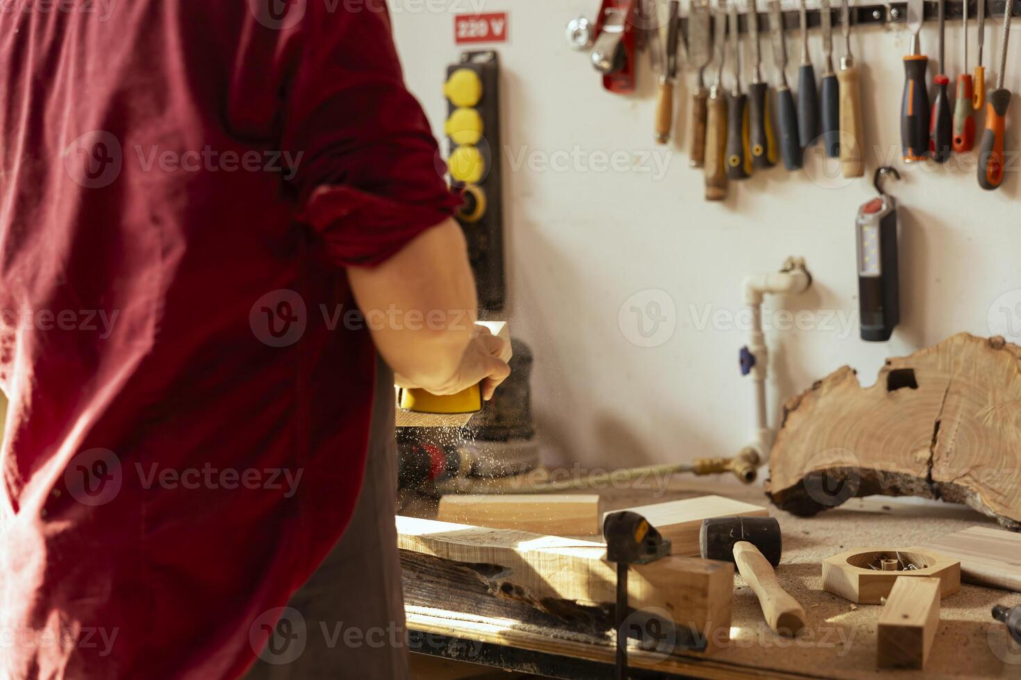 Man in studio with woodworking tools in background using sandpaper for sanding wooden surface. Woodworking expert using abrasive sponge to fix damages suffered by piece of wood photo