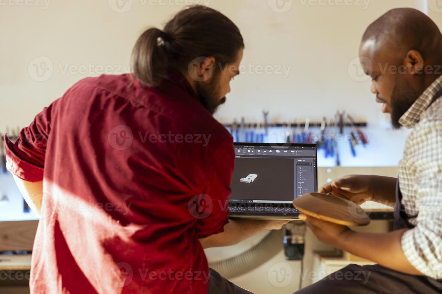 Woodworker looking over blueprints on laptop in CAD software with apprentice. Manufacturer and coworker designing custom 3D furniture on notebook in studio, preparing for customer order photo